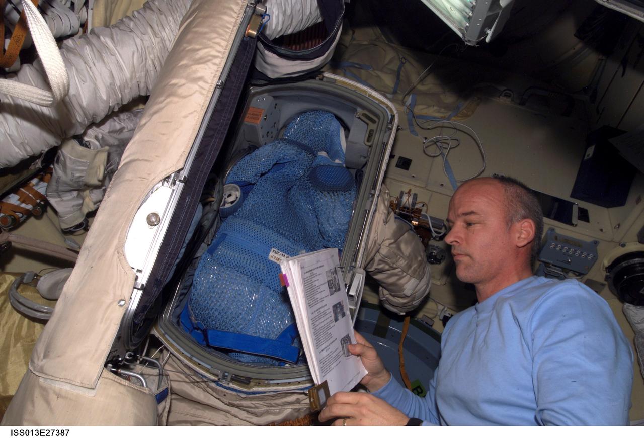 ISS013-E-27387 (26 May 2006) --- Astronaut Jeffrey N. Williams, Expedition 13 NASA space station science officer and flight engineer, looks over a procedures checklist near a Russian Orlan spacesuit in the Zvezda Service Module of the International Space Station.