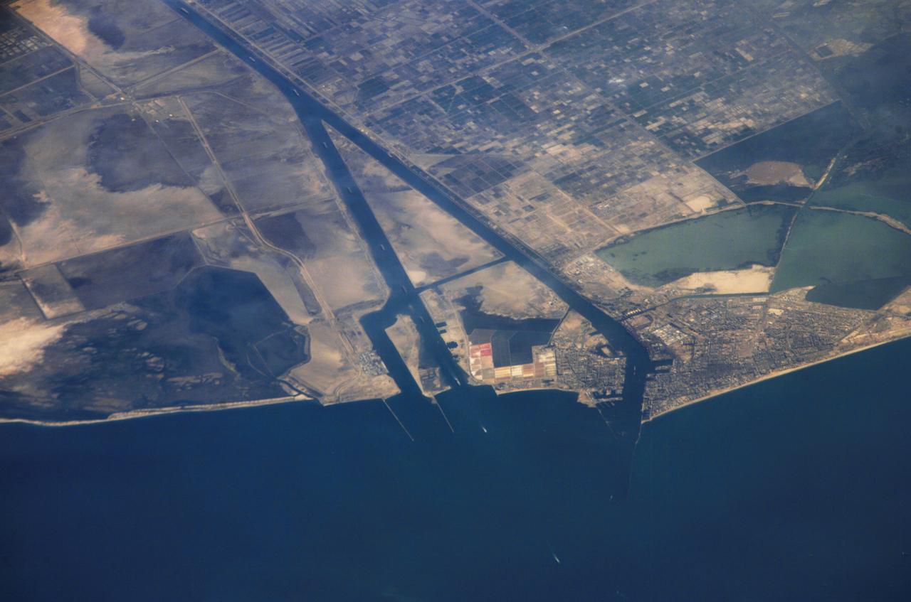 ISS013-E-44847 (30 June 2006) --- Ship traffic on the Suez Canal, Egypt is featured in this image photographed by an Expedition 13 crewmember on the International Space Station. This oblique photograph captures a northbound convoy of cargo ships entering the Mediterranean Sea from the Suez Canal in Egypt (leftmost canal branch at image center). Oblique images are taken at an angle other than vertical, or nadir -- looking down a line connecting the station to the point on the Earth's surface directly below it -- and this provides a sense of perspective. In this case, the station was located above the eastern coast of Cyprus and the crewmember was looking at Egypt to the southwest. Regions of reduced clarity in the image are caused by thin variable cloud cover. The Suez Canal connects Port Said on the Mediterranean Sea with the port of Suez on the Red Sea, and provides an essentially direct route for transport of goods between Europe and Asia. The Canal is 163 kilometers long and 300 meters wide at its narrowest point -- sufficiently wide for ships as large as aircraft carriers to traverse it. Transit time from end to end is 14 hours on average.