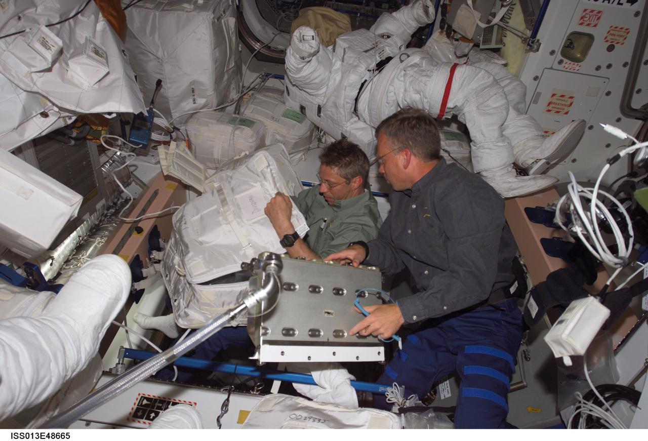 ISS013-E-48665 (6 July 2006) --- European Space Agency astronaut Thomas Reiter (left) and astronaut Steven W. Lindsey work in the Quest airlock aboard the International Space Station during their first day on the orbital outpost. Lindsey, STS-121 commander, will spend a little over a week there, and Reiter is scheduled for a six month stay. Astronaut Piers J. Sellers' extravehicular mobility unit space suit for the scheduled July 8 space walk is in the background.