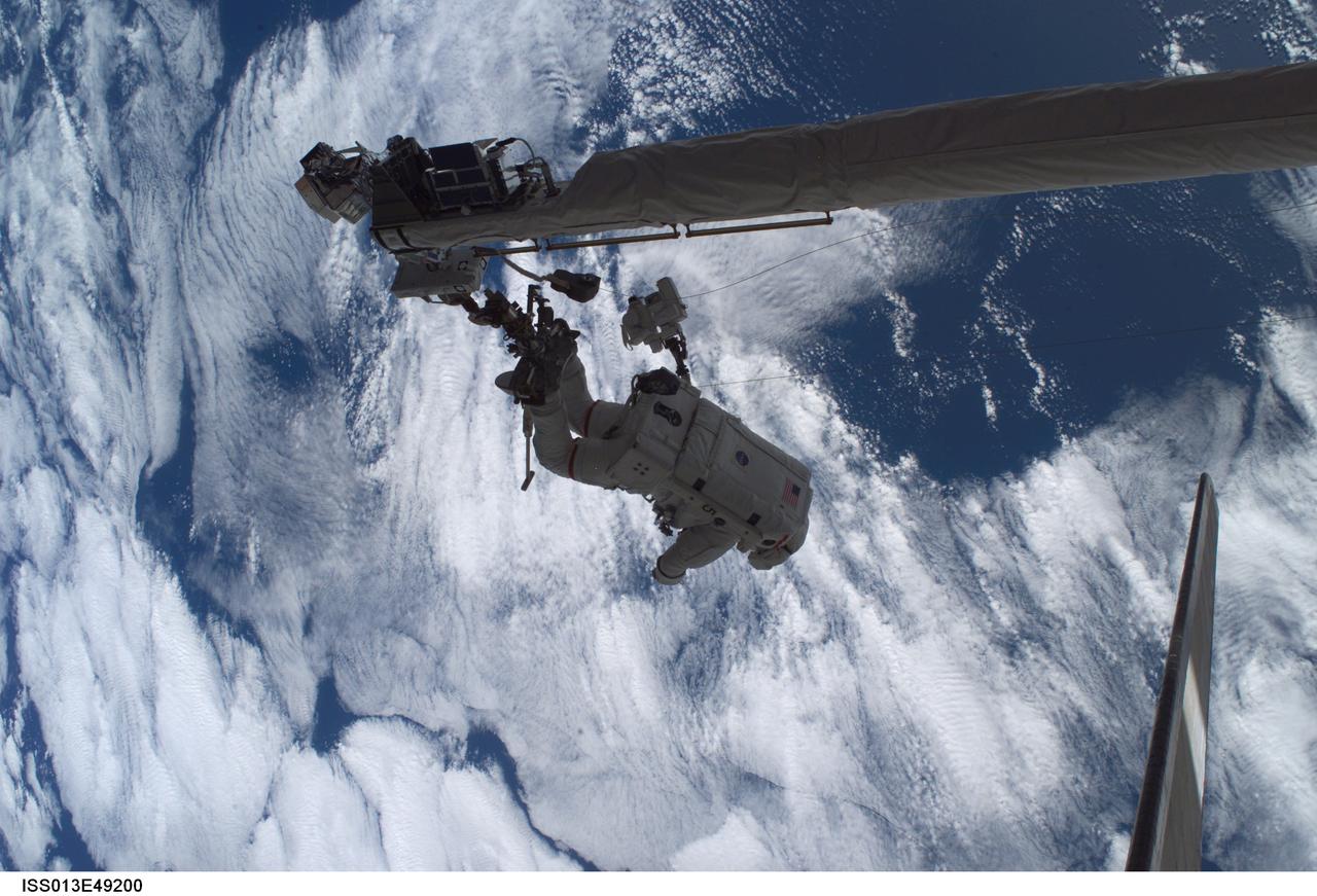 ISS013-E-49200 (8 July 2006) --- Anchored to the Space Shuttle Discovery's Remote Manipulator System/Orbiter Boom Sensor System (RMS/OBSS) foot restraint, astronaut Piers J. Sellers, STS-121 mission specialist, participates in the mission's first session of extravehicular activity (EVA) while the shuttle was docked with the International Space Station. Discovery's vertical stabilizer is at right. A cloud-covered Earth provides the backdrop for the scene.