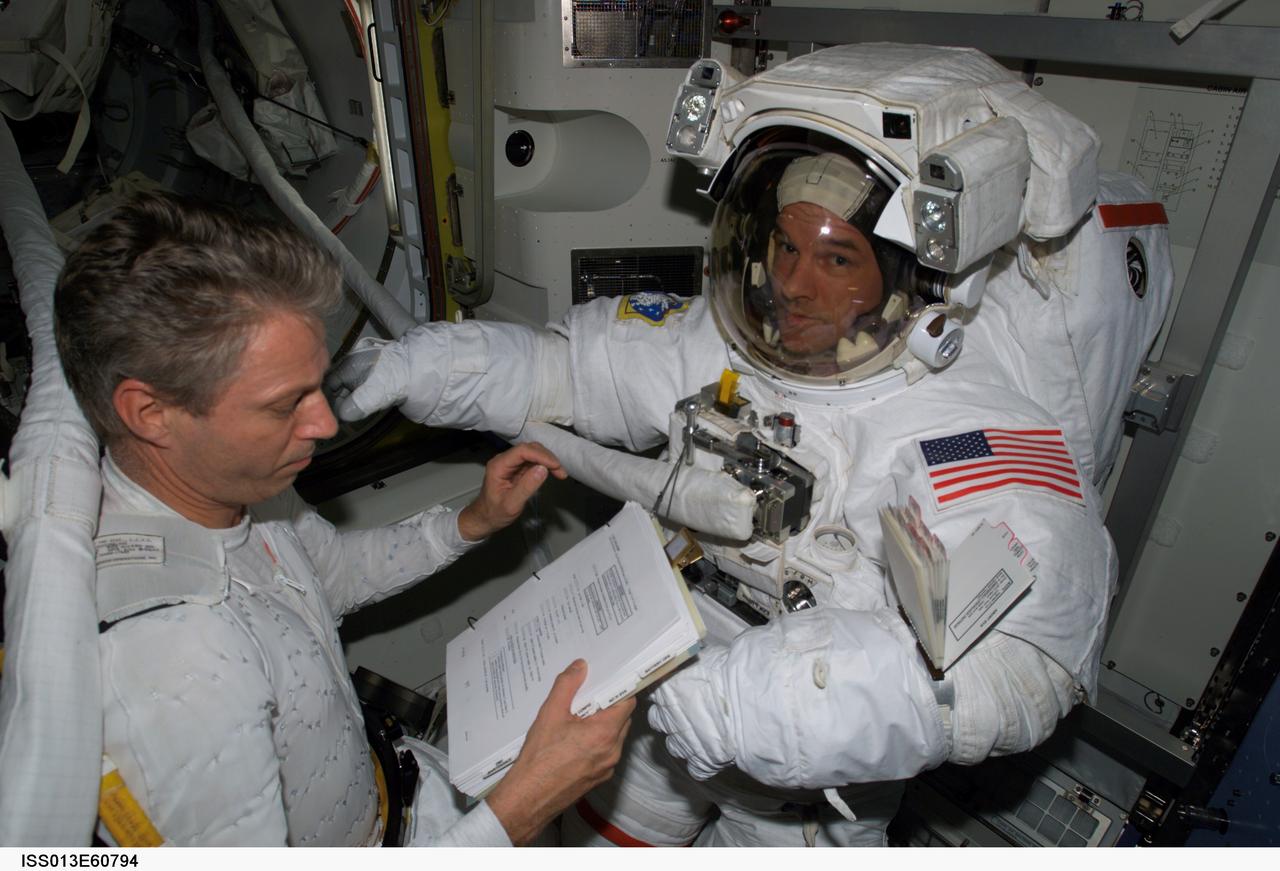 ISS013-E-60794 (28 July 2006) --- European Space Agency (ESA) astronaut Thomas Reiter (left), Expedition 13 flight engineer, looks over a procedures checklist as he assists astronaut Jeffrey N. Williams, NASA space station science officer and flight engineer, with his Extravehicular Mobility Unit (EMU) space suit in the Quest Airlock of the International Space Station. The crew is preparing for a session of extravehicular activity (EVA) scheduled for Thursday, Aug. 3, 2006. Reiter is attired in a liquid cooling and ventilation garment that complements the EMU space suit.