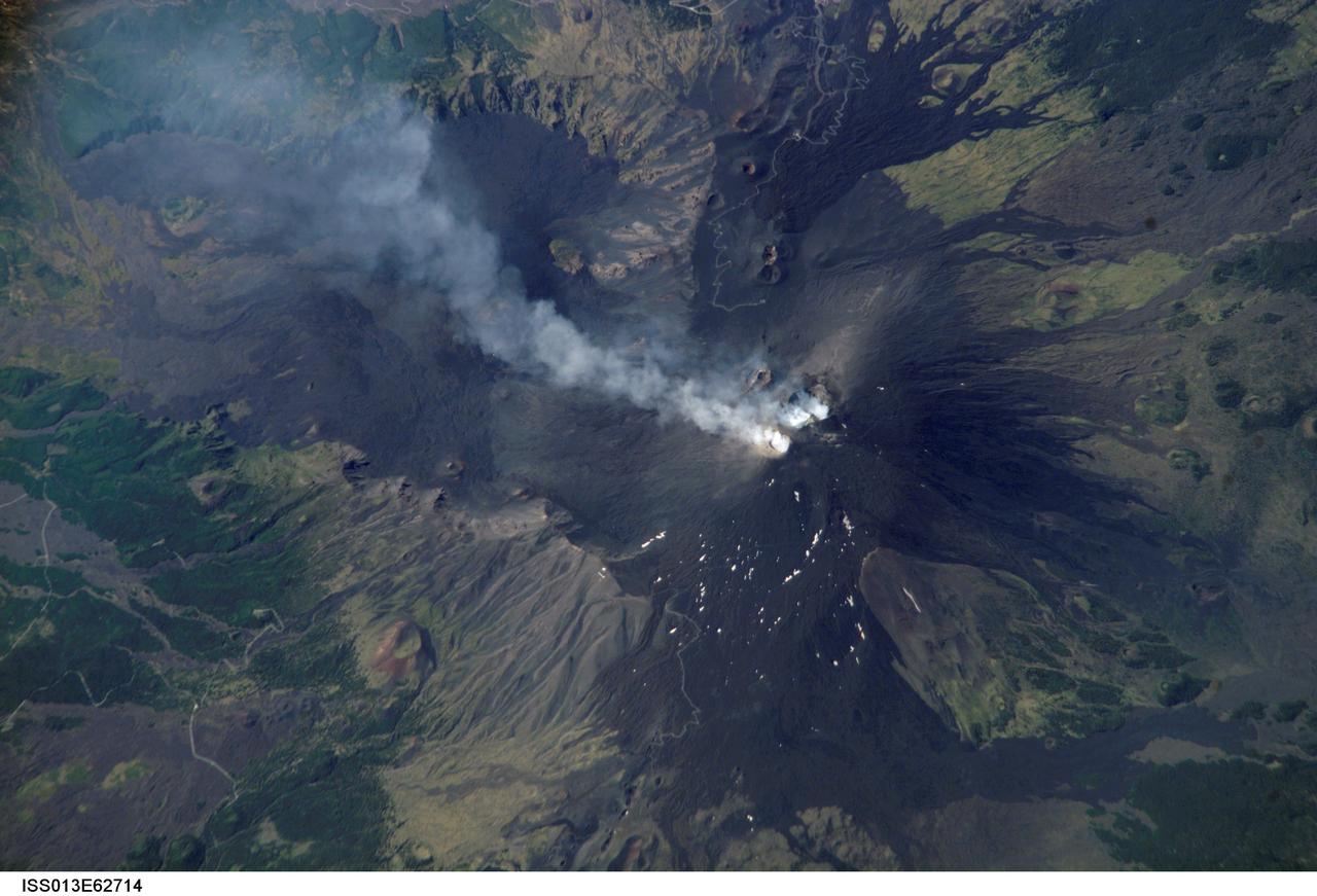 ISS013-E-62714 (2 Aug. 2006) --- Mt. Etna Summit Plumes, Sicily is featured in this image photographed by an Expedition 13 crewmember on the International Space Station. One of the most consistently active volcanoes in the world is Sicily's Mt. Etna, which has a historical record of eruptions dating back to 1500 B.C. This image captures plumes of steam and possible minor ash originating from summit craters on the mountain -- the Northeast Crater and Central Crater, which includes two secondary craters (Voragine and Bocca Nuova). Explosions were heard from the rim of the Northeast Crater on July 26, and scientists suspect that these plumes are a continuation of that activity. The massive 3350 meter high volcano is located approximately 24 kilometers to the north of Catania, the second largest city in Sicily, and dominates the northern skyline. Much of Etna's surface is comprised of numerous generations of dark basaltic lava flows, as can be seen extended outwards from the summit craters. Fertile soils developed on older flows are marked by green vegetation. While the current explosive eruptions of Etna tend to occur at the summit, lava flows generally erupt through fissures lower down on the flanks of the volcano. Many of the lava flow vents are marked by cinder cones on the flanks of Mt. Etna. Scientists have noted evidence of larger eruptive events as well. The Valle Del Bove to the south-southeast of the summit is a caldera formed by the emptying of a subsurface magma chamber during a large eruptive event -- once the magma chamber was emptied, the overlaying roof material collapsed downwards.