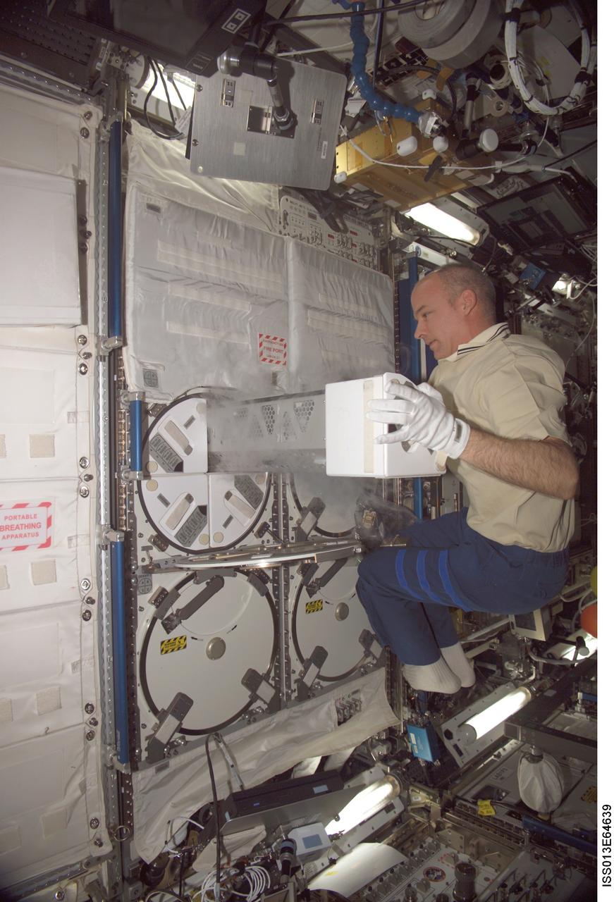 ISS013-E-64639 (2 Aug. 2006) --- Astronaut Jeffrey N. Williams, Expedition 13 NASA space station science officer and flight engineer, inserts a sample of the Passive Observatories for Experimental Microbial Systems in Micro-G (POEMS) payload in the Minus Eighty Degree Laboratory Freezer for ISS (MELFI) in the Destiny laboratory of the International Space Station. MELFI is a low temperature freezer facility with nominal operating temperatures of -80, -26 and +4 degrees Celsius that will preserve experiment materials over long periods.