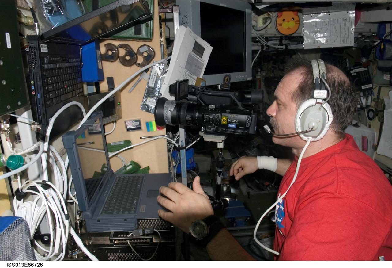 ISS013-E-66726 (August 2006) --- Cosmonaut Pavel V. Vinogradov, Expedition 13 commander representing Russia's Federal Space Agency, wears a communication system headset while using a video camcorder and computer in the Zvezda Service Module of the International Space Station.