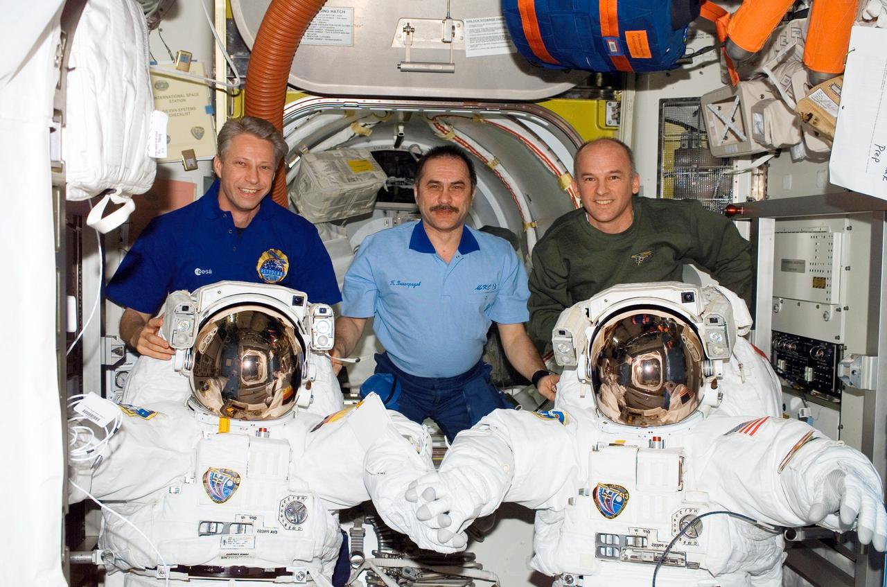 ISS013-E-66729 (13 Aug. 2006) --- European Space Agency (ESA) astronaut Thomas Reiter (left), Expedition 13 flight engineer; cosmonaut Pavel V. Vinogradov, commander representing Russia's Federal Space Agency; and Jeffrey N. Williams, NASA space station science officer and flight engineer, pose for a photo with two Extravehicular Mobility Unit (EMU) spacesuits in the Quest Airlock of the International Space Station.