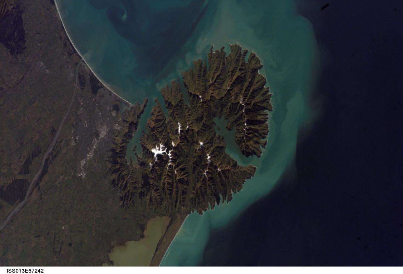 ISS013-E-67242 (15 Aug. 2006) --- Christchurch, New Zealand is featured in this image photographed by an Expedition 13 crewmember on the International Space Station. Snow highlights the peaks of the Banks Peninsula to the southeast of the city. The Peninsula has a radically different landscape compared to the adjoining flat Canterbury Plains on which Christchurch is situated. This is a result of the geology of the Banks Peninsula -- it is formed from the overlapping cones of the extinct Lyttelton and Akaroa volcanoes. Subsequent erosion of the cones formed the heavily dissected terrain visible in the image, and sea level rise led to the creation of several harbors around the Peninsula. Erosion continues unabated today, as evidenced by the apron of greenish blue sediment-laden waters surrounding the Banks Peninsula. Other features of interest in the image include the braided Waimakariri River to the north-northwest of the city, and the greenish brown waters of Lake Ellesmere. The coloration of the water is due both to its shallow depth (1.4 meters average) and its high concentrations of nitrogen and phosphorus - conditions which lead to a high abundance of green algae.