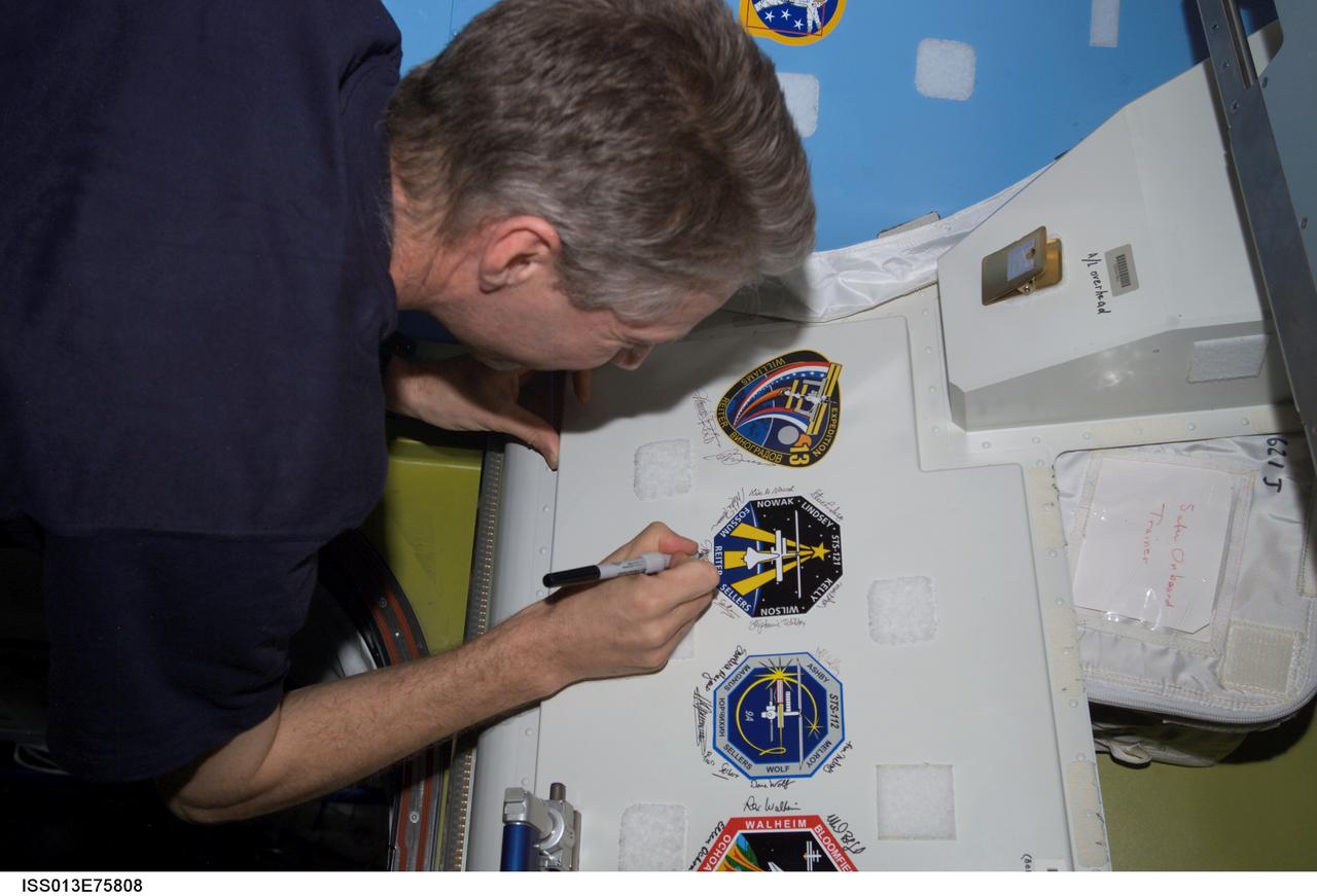 ISS013-E-75808 (4 Sept. 2006) --- European Space Agency (ESA) astronaut Thomas Reiter, Expedition 13 flight engineer, signs the Expedition 13 and STS-121 patches, which were added to the growing collection of insignias representing crews who have performed spacewalks from the Quest Airlock of the International Space Station.