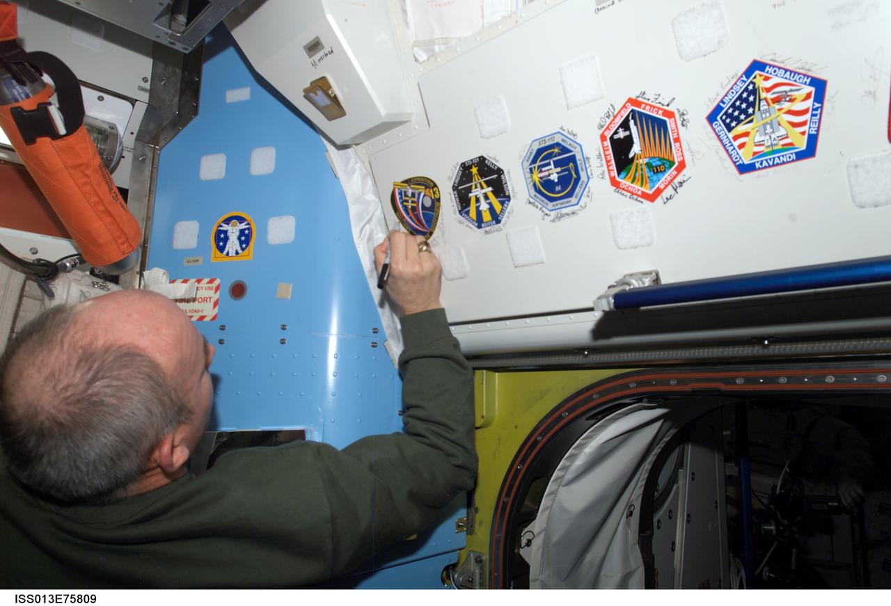 ISS013-E-75809 (4 Sept. 2006) --- Astronaut Jeffrey N. Williams, Expedition 13 NASA space station science officer and flight engineer, signs the Expedition 13 patch, which was added to the growing collection of insignias representing crews who have performed spacewalks from the Quest Airlock of the International Space Station.