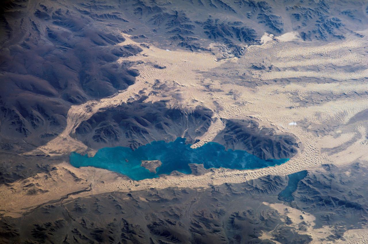 ISS013-E-78506 (7 Sept. 2006) --- Sand dunes near Mongolia's Har Lake are featured in this image photographed by an Expedition 13 crewmember on the International Space Station. Har (or Black) Lake is located in the western part of the country within the Valley of Lakes--part of a system of closed basins that stretches across central Asia. According to scientists, these basins are the remnants of larger paleolakes that had begun to shrink in size by approximately five thousand years ago as regional climate became drier. Today, the Valley of Lakes is an important ecological resource for study of steppe grasslands, and as resting points for large numbers of migratory birds. Portions of the basin are designated as national parks or other protected areas, and Har Lake itself is an ecotourism destination (usually by horseback). This oblique view captures the dynamic nature of the landscape of Har Lake. The lake is encircled by sand dune fields which encroach on the lower slopes of the Tobhata Mountains to the west and south. Gaps in the mountains have been exploited by sand dunes moving eastward (indicating westerly winds) -- the most striking example being a series of dunes entering Har Lake along its southwestern shoreline. Here, the dune forms reflect the channeling of winds through the break in the mountain ridgeline, leading to dune crests oriented transverse to northwesterly winds. Another well-developed line of dunes is visible between Har and Baga Lakes. While these dunes appear to cut across a lake surface, the dunes have in fact moved across a narrow stream channel.