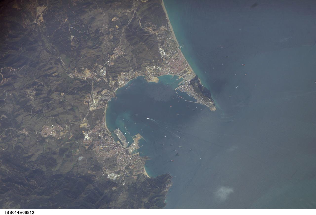 ISS014-E-06812 (30 Oct. 2006) --- Gibraltar Bay, located near the southernmost tip of the Iberian Peninsula in the western Mediterranean Sea, is featured in this image photographed by an Expedition 14 crewmember on the International Space Station. According to scientists, the famous Rock of Gibraltar that forms the northeastern border of the Bay is formed of Jurassic seafloor sediments that were lithified to form limestone (a rock formed predominantly of the mineral calcite) and subsequently uplifted as a result of collision of the African and Eurasian tectonic plates. The cities of La Linea and Algeciras bordering the Bay -- together with petroleum-processing facilities along the northern Bay shoreline -- are part of Spain, whereas the city of Gibraltar itself (to the west of and including the Rock) is under the jurisdiction of the United Kingdom. The protected waters of the Bay and its proximity to Africa and the Strait of Gibraltar as the gateway between the Atlantic and Mediterranean contribute to the region's past and current strategic and economic importance. Numerous ships and several ship wakes are visible within the Bay; the majority of these are freighters and cargo tankers accessing the petroleum facilities. Ships nearer to the Rock are more likely cruise ships, as Gibraltar is a popular destination for tourists. Partial sunglint within the Bay highlights surface water roughened by winds funneled into the Bay by the surrounding highlands -- one such area is visible directly to the west of La Linea.