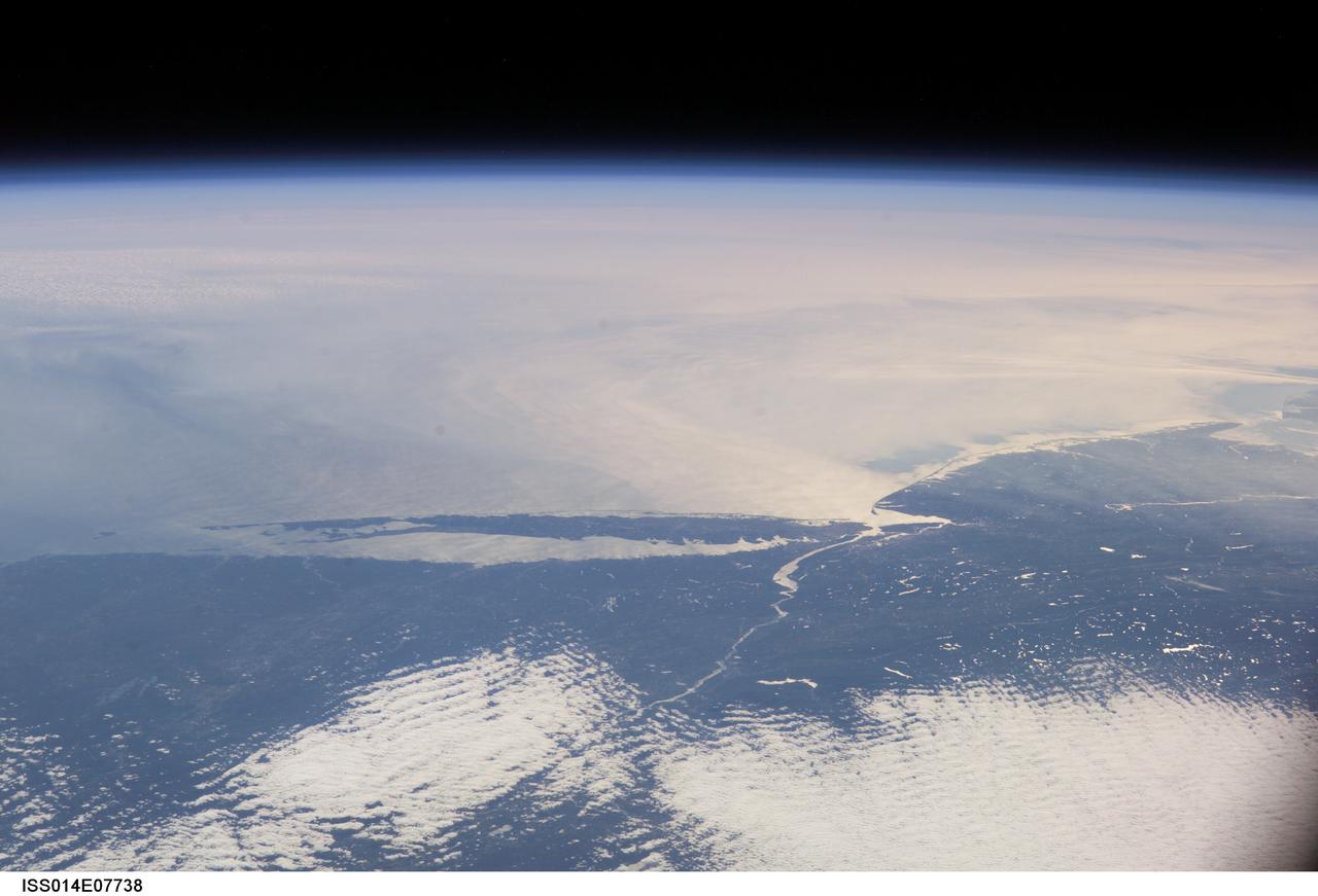 ISS014-E-07738 (10 Nov. 2006) --- This image featuring a southeast-looking view of the Long Island Sound and New Jersey coast, with the lower Hudson River and New York Bay in the area of brightest sunglint was photographed by an Expedition 14 crewmember on the International Space Station. On the far right a gray haze can be seen streaming out to sea offshore of New Jersey, where it becomes harder to see.  In fact haze covers most of the visible area offshore, partly obscuring the sea surface. By contrast, clouds look quite different from haze according to scientists. Clouds usually have sharp margins and are pure white, as clouds at the bottom show. Industrial haze is grayer and more diffuse, and is typical of the air over the Northeast. Flow lines show that winds are transporting the haze in clockwise fashion--i.e. bending south--which in turn signifies that a high pressure system was operating on that day, centered roughly over the coast. High pressure systems are notorious for promoting smog events because they bring clear skies, and sunlight promotes smog formation. Highs also concentrate polluted surface layers near the ground.