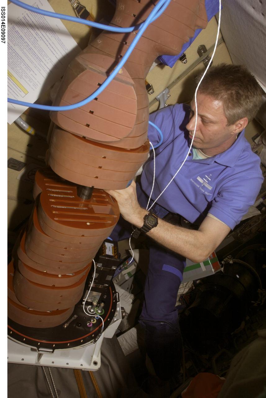 ISS014-E-09097 (December 2006) --- European Space Agency (ESA) astronaut Thomas Reiter, Expedition 14 flight engineer, works with the European Matroshka-R Phantom experiment in the Zvezda Service Module of the International Space Station. Matroshka, the name for the traditional Russian set of nestling dolls, is an antroph-amorphous model of a human torso designed for radiation studies. The activity, supported by ground specialist tag-up, requires equipping the torso's individual horizontal slice-like layers with 356 thermo luminescent detectors (TLDs) and five nuclear radiation tracking detectors (NTDPs). The mannequin was then to be reassembled, covered with poncho and hood and installed in the Pirs Docking Compartment for studies of on-orbit radiation and long-term dose accumulation.