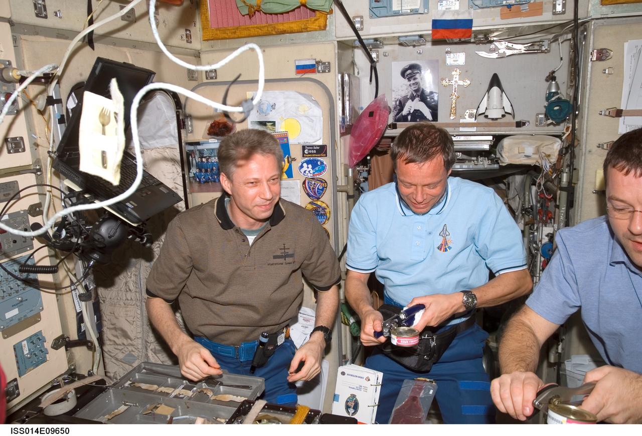 ISS014-E-09650 (13 Dec. 2006) --- European Space Agency (ESA) astronauts Thomas Reiter (left) and Christer Fuglesang; and astronaut Nicholas J. M. Patrick (partially out of frame), all STS-116 mission specialists, share a meal at the galley in the Zvezda Service Module of the International Space Station.