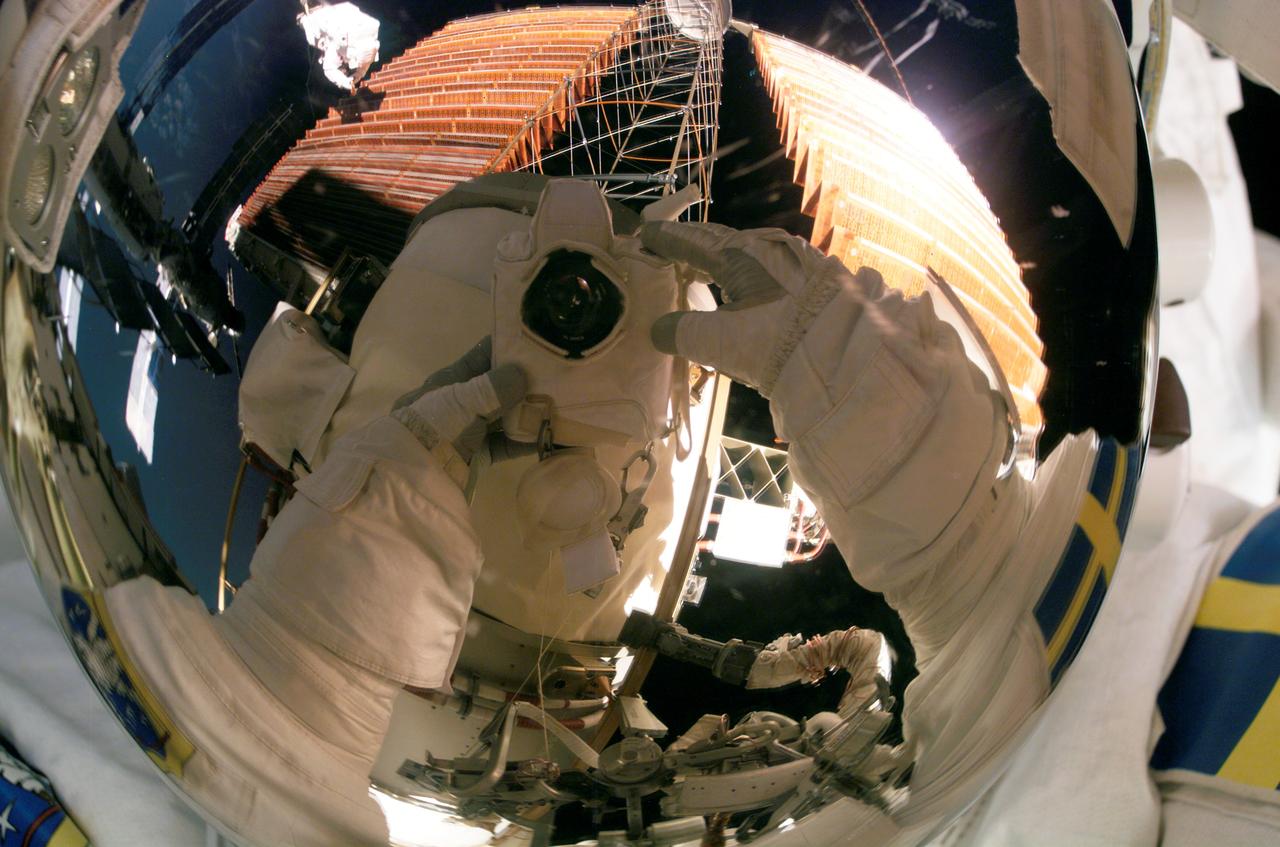 ISS014-E-10089 (18 Dec. 2006) --- European Space Agency (ESA) astronaut Christer Fuglesang, STS-116 mission specialist, uses a digital still camera to expose a photo of his helmet visor during the mission's fourth session of extravehicular activity (EVA) while Space Shuttle Discovery was docked with the International Space Station. Also visible in the reflections in the visor is astronaut Robert L. Curbeam Jr., mission specialist, as he works with the port overhead solar array wing on the station's P6 truss. The spacewalkers worked in tandem, using specially prepared, tape-insulated tools, to guide the array wing neatly inside its blanket box during the 6-hour, 38-minute spacewalk.