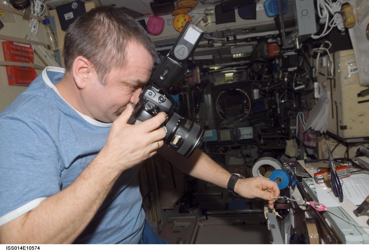 ISS014-E-10574 (28 Dec. 2006) --- Cosmonaut Mikhail Tyurin, Expedition 14 flight engineer representing Russia's Federal Space Agency, using a digital still photo camera, documents repair work done on a frayed cable in the Zvezda Service Module of the International Space Station.