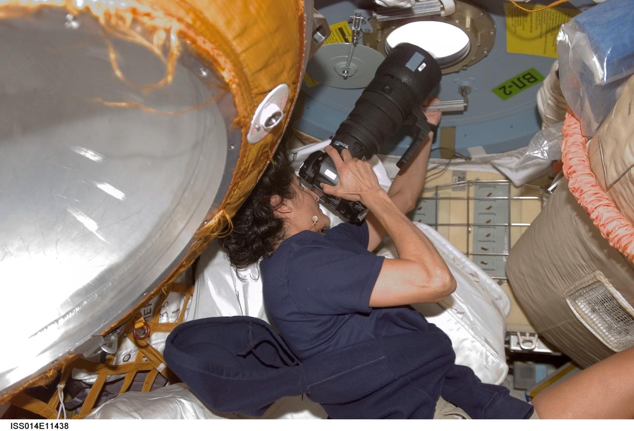ISS014-E-11438 (10 Jan. 2007) --- Astronaut Sunita L. Williams, Expedition 14 flight engineer, uses a still camera at a window in the Pirs Docking Compartment of the International Space Station.