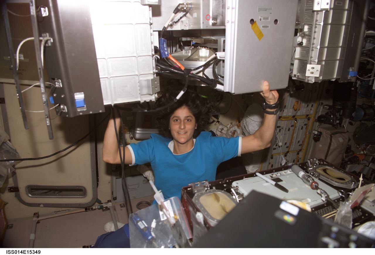 ISS014-E-15349 (27 Feb. 2007) --- Assisted by the weightlessness of space, astronaut Sunita L. Williams, Expedition 14 flight engineer, hoists the Treadmill Vibration Isolation System (TVIS). She took a moment to pose for a photo during routine in-flight maintenance (IFM) on TVIS in the Zvezda Service Module of the International Space Station.