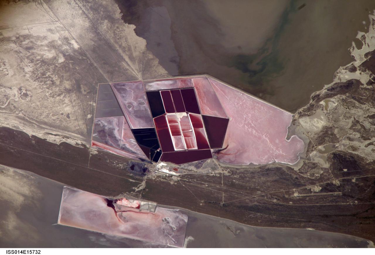 ISS014-E-15732 (1 March 2007) --- Salt ponds of Botswana are featured in this image photographed by an Expedition 14 crewmember on the International Space Station. This recent, detailed view shows the salt ponds of one of Africa's major producers of soda ash (sodium carbonate) and salt. Soda ash is used for glass making, in metallurgy, in the detergent industry, and in chemical manufacture. The image shows a small part of the great salt flats of central Botswana known as the Makgadikgadi Salt Pans. The soda ash and salt are both mainly exported (since 1989) to most countries in southern and central Africa. Brines from just beneath the pan floor are evaporated to produce the soda ash and salt -- a process for which the semiarid climate of Botswana is ideal.  Red salt-loving algae in the ponds indicate that the salinity of the evaporating brines is medium to high. The salt pans of Botswana--a prominent visual photo target of interest for astronauts aboard the station--lie at the low point of a vast shallow continental basin. Rivers draining from as far away as central Angola - more than 1,000 kilometers away - supply water to the pans. According to scientists, during several wet climatic phases in the recent geological past the pans were permanently filled with water, for thousands of years, only to dry out when climates fluctuated to drier conditions. During dry phases water only reaches the pans underground. These are the brines that support the ash and salt industry. During wet phases when open water exists, beach ridges are constructed by wave action. One of these crosses the lower part of the view.