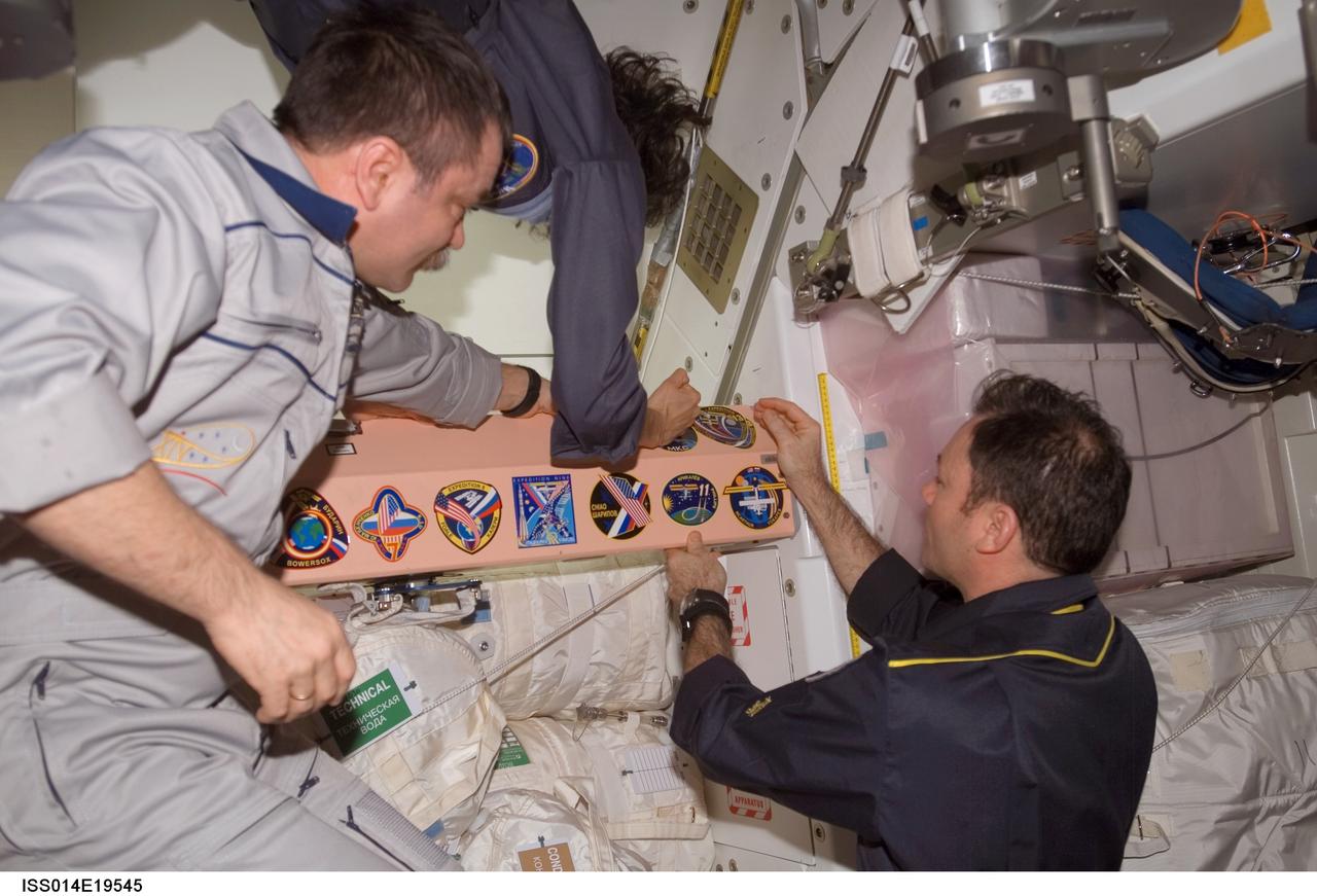 ISS014-E-19545 (17 April 2007) --- Astronauts Michael E. Lopez-Alegria (right), Expedition 14 commander and NASA space station science officer; Sunita L. Williams, flight engineer; and cosmonaut Mikhail Tyurin (left), flight engineer representing Russia's Federal Space Agency, add the Expedition 14 patch to the Unity node's growing collection of insignias representing crews who have lived and worked on the International Space Station.