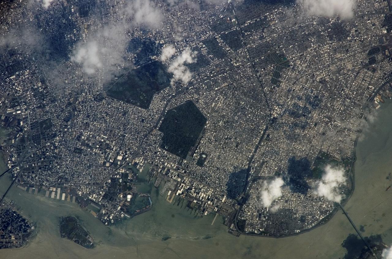 ISS015-E-05483 (28 April 2007) --- Brooklyn, New York waterfront is featured in this image photographed by an Expedition 15 crewmember on the International Space Station. This view illustrates the dense urban fabric of Brooklyn, New York City's largest borough (population of 2.6 million), characterized by the regular pattern of highly reflective building rooftops (white). Two main arteries from Manhattan into Brooklyn, the famous Brooklyn Bridge and neighboring Manhattan Bridge, cross the East River along the left (north) side of the image. The dense built-up fabric contrasts with the East River and Upper New York Bay (bottom center) waterfront areas, recognizable by docks and large industrial loading facilities that extend across the bottom center from left to right. Much of the shipping traffic has moved to the New Jersey side of New York Bay--this has spurred dismantling and redevelopment of the historic dockyards and waterfront warehouses into residential properties. However, efforts to conserve historic buildings are also ongoing. The original name for Brooklyn, Breukelen, means "broken land" in Dutch--perhaps in recognition of the highly mixed deposits (boulders, sand, silt, and clay) left behind by the Wisconsin glacier between 20,000--90,000 years ago, according to scientists. These deposits form much of Long Island, of which Brooklyn occupies the western tip. This image features one of Brooklyn's largest green spaces, the Green-Wood Cemetery. Today, the cemetery functions as both a natural park and a place of internment. The green tree canopy of the Cemetery contrasts sharply with the surrounding urban land cover, is an Audubon Sanctuary, and provides the final resting place for many 19th and 20th century New York celebrities. Also visible in the image is Governor's Island, which served as a strategic military installation for the US Army (1783--1966) and a major US Coast Guard installation (1966--1996). Today the historic fortifications on the island and their surroundings comprise the Governors Island National Monument.