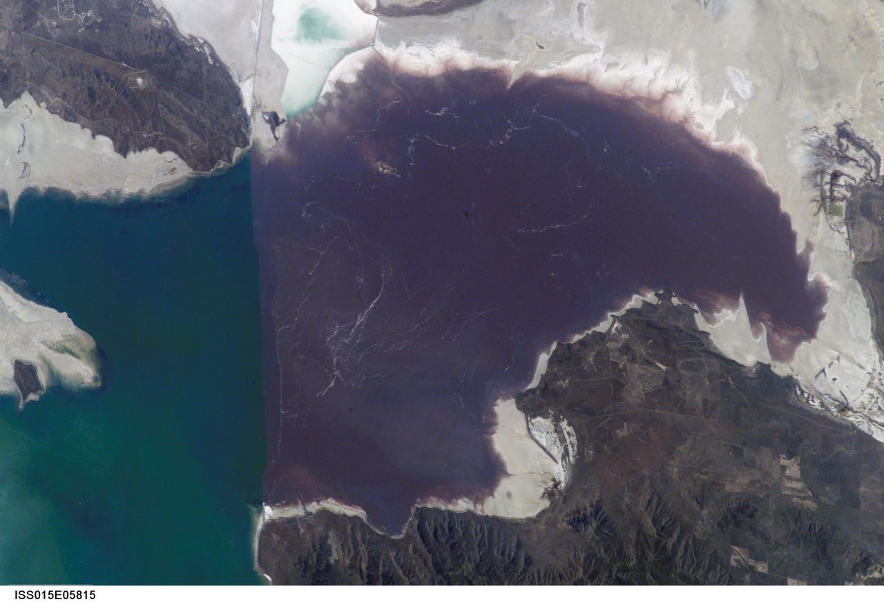 ISS015-E-05815 (30 April 2007) --- Algae in Great Salt Lake, Utah is featured in this image photographed by an Expedition 15 crewmember on the International Space Station. According to scientists, the Great Salt Lake of northern Utah is a remnant of glacial Lake Bonneville that extended over much of present-day western Utah, and into the neighboring states of Nevada and Idaho, approximately 32,000 to 14,000 years ago. During this time, the peaks of adjacent ranges such as the Promontory and Lakeside Mountains were most likely islands. As climate warmed and precipitation decreased in the region, glaciers that fed melt-water to Lake Bonneville disappeared, and the lake began to dry up. The present-day Great Salt Lake is a terminal lake in that water does not flow out of the lake basin. Water loss through the year is due primarily to evaporation, and when this loss exceeds input of water from rivers, streams, precipitation, and groundwater the lake level decreases. This is particularly evident during droughts. This process of evaporation, together with the relatively shallow water levels (maximum lake depth is around 33 feet), has led to increased salinity (dissolved salt content) of the lake waters. The north arm of the Lake, displayed in this image, typically has twice the salinity of the rest of the lake due to impoundment of water by a railroad causeway that crosses the lake from east to west. This restriction of water flow has led to a striking division in the types of algae and bacteria found in the north and south arms of the lake. In the northern arm (north of the causeway), the red algae Dunaliella Salina and the bacterial species Halo bacterium produce a pronounced reddish cast to the water, whereas the south arm (south of the causeway) is dominated by green algae such as Dunaliella viridis. The Great Salt Lake also supports brine shrimp and brine flies; and is a major stopover point for migratory birds including avocets, stilts, and plovers.
