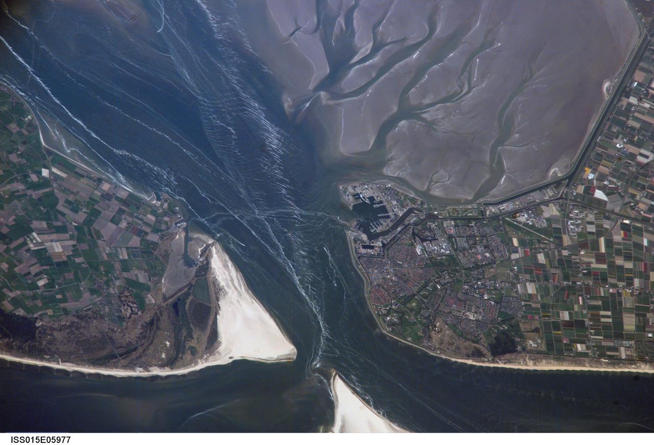 ISS015-E-05977 (1 May 2007) --- Den Helder, Netherlands is featured in this image photographed by an Expedition 15 crewmember on the International Space Station. The city and harbor of Den Helder in the northern Netherlands has been the home port of the Dutch Royal Navy for over 175 years. Its favorable location provides access to the North Sea, and has made it an important commercial shipping port in addition to its strategic role. Bright red agricultural fields to the south of Den Helder indicate another noteworthy aspect of the region--commercial farming of tulips and hyacinth. This image is an oblique view--the camera is oriented at an angle relative to "straight down"--of the Den Helder region taken from the space station, which was located to the southeast, near Dulmen, Germany (approximately 225 kilometers away in terms of ground distance) when the image was acquired. In addition to the manmade structures of the Den Helder urban area (reddish gray to gray street grids) and dockyards to the east of the city, several striking geomorphic features are visible. The extensive gray mudflats, with their prominent branching pattern (top right), indicate that this image was acquired at low tide, and suggest the general low elevation of the region. Parallel wave patterns along the mudflats and in the Marsdiep strait are formed as water interacts with the sea bottom between Den Helder and Texel Island during tidal flow. Some ship wakes are also visible. According to scientists, the bright white-gray triangular region at the southern tip of Texel Island (bottom center) is a dune field, consisting mainly of eolian (windborne) sands deposited during the last Ice Age. Subsequent sea level rise and shoreline processes have mobilized and re-deposited these sands into their current configuration -- including a new dune field island to the southwest of Texel (bottom center).