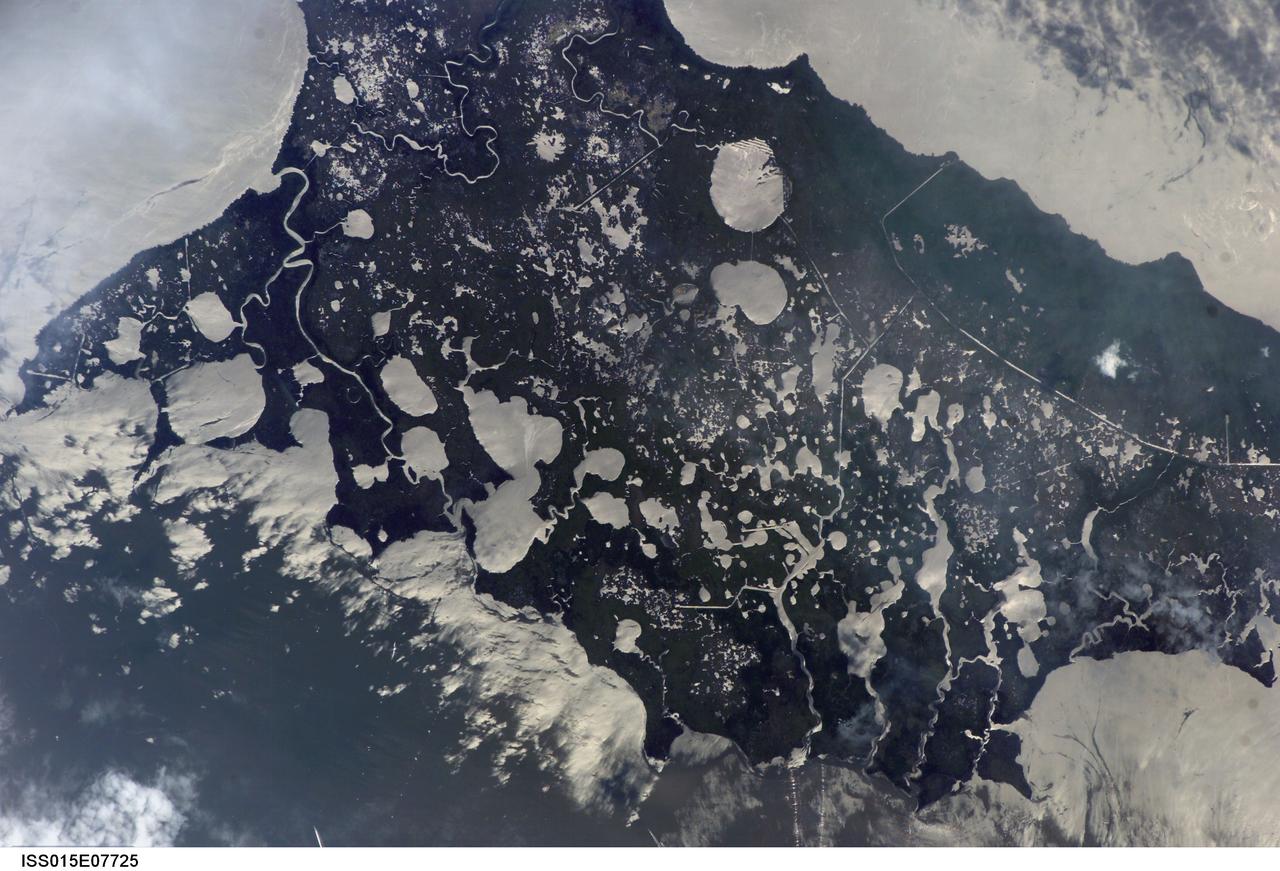 ISS015-E-07725 (11 May 2007) --- Marsh Island, Louisiana is featured in this image photographed by an Expedition 15 crewmember on the International Space Station. Marsh Island, located along the southwestern coastline of Louisiana, is a remnant of an abandoned lobe of the Mississippi River Delta formed approximately 5000-7500 years before the present day, according to scientists. It is composed primarily of organic-rich muds and brackish marsh vegetation (some peat -- semiconsolidated plant and organic matter -- is also present). The intricate lake, pond and stream network of the island is highlighted in this image by silver-gray sunglint -- light reflected off of water surfaces directly back to the crewmember on the space station. Sunglint also illuminates water surfaces in the adjacent Gulf of Mexico and West Cote Blanche Bay -- variations in intensity of reflectance in these water bodies is due to surface roughness (often related to wind-driven waves or currents) and the presence of surfactants that can change the surface properties of the water. Marsh Island is a popular fishing, shrimping and birding location. The island has experienced significant loss of vegetation and land area -- nearly 3,000 hectares (7,000 acres) - due to erosion, with a corresponding loss of habitat for local and migratory birds, shrimp, alligators and deer. While Marsh Island is uninhabited, it has been the focus of intensive development for management of erosion, such as revegetation of deteriorated marsh areas. Leveed canals (straight silver-gray water features) help drain areas for above-surface revegetation, while sill dams help stabilize water levels and foster regrowth of important subsurface vegetation such as widgeongrass.