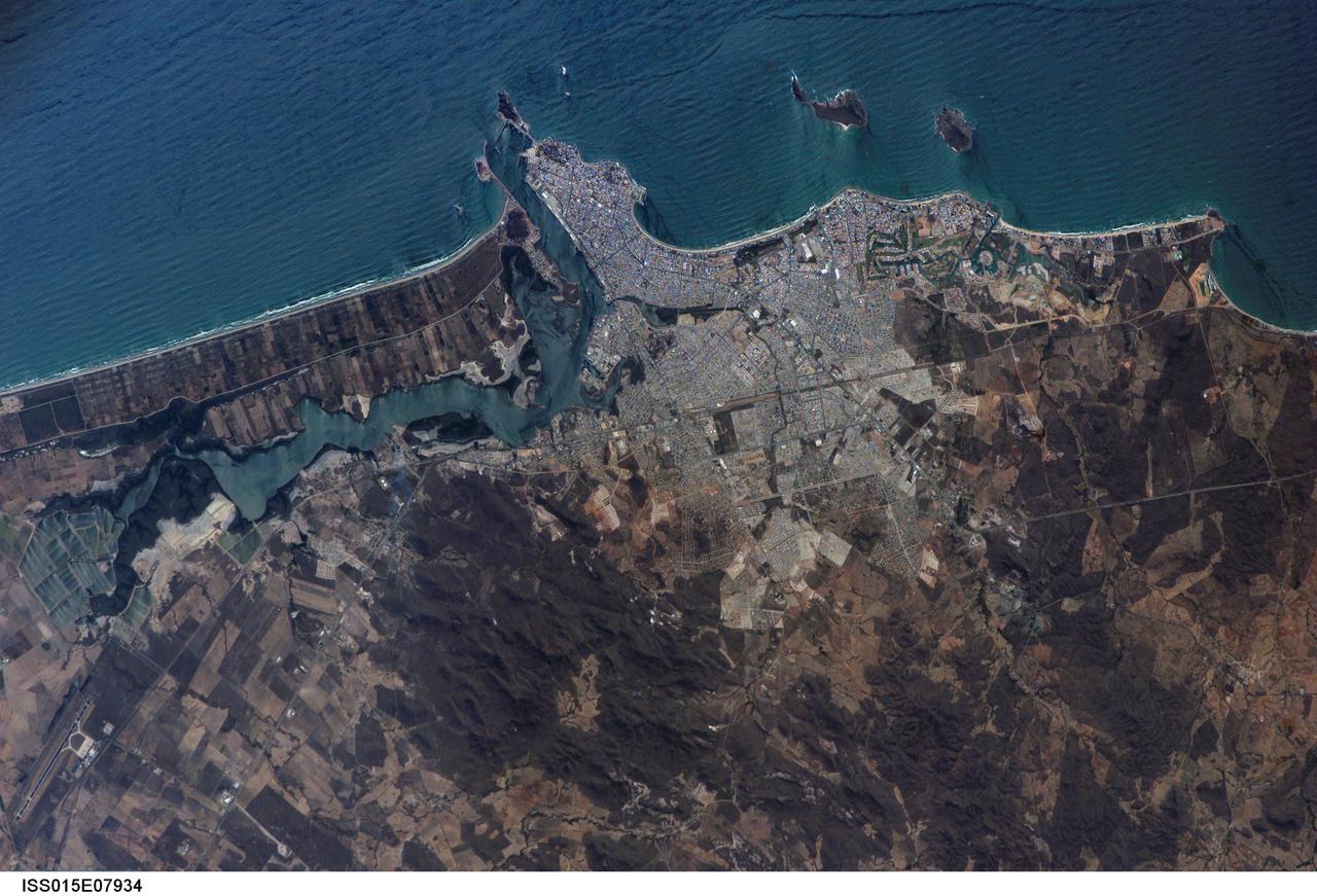 ISS015-E-07934 (13 May 2007) --- Mazatlan, Mexico is featured in this image photographed by an Expedition 15 crewmember on the International Space Station. Mazatlan is Mexico's largest port, situated on one of the best estuaries on Mexico's Pacific coast, illustrated well in this image. Docks and naval yards line the north side of the estuary. The city itself appears as a series of light-toned city blocks covering the center of the image. Mazatlan (population of 352,000 in 2005) is growing northward from the downtown peninsula, with tourist beaches backed by hotels, and a marina and golf courses just beyond. No city growth yet appears on the south side the estuary where farm lands can be seen. The famous Faro Lighthouse occupies the top of a steep island--now connected by a bridge to the mainland--at the mouth of the estuary (top center). The Faro Lighthouse is the second tallest in the world behind Gibraltar's. The wide, straight, almost vertical line of the railroad appears to bisect the picture. This image shows sea features well, primarily ocean swells coming in from the southwest, which appear as a series of parallel lines covering the entire sea surface in this view. An oil slick offshore of the tourist beaches appears as a dark line along the left side of the image.