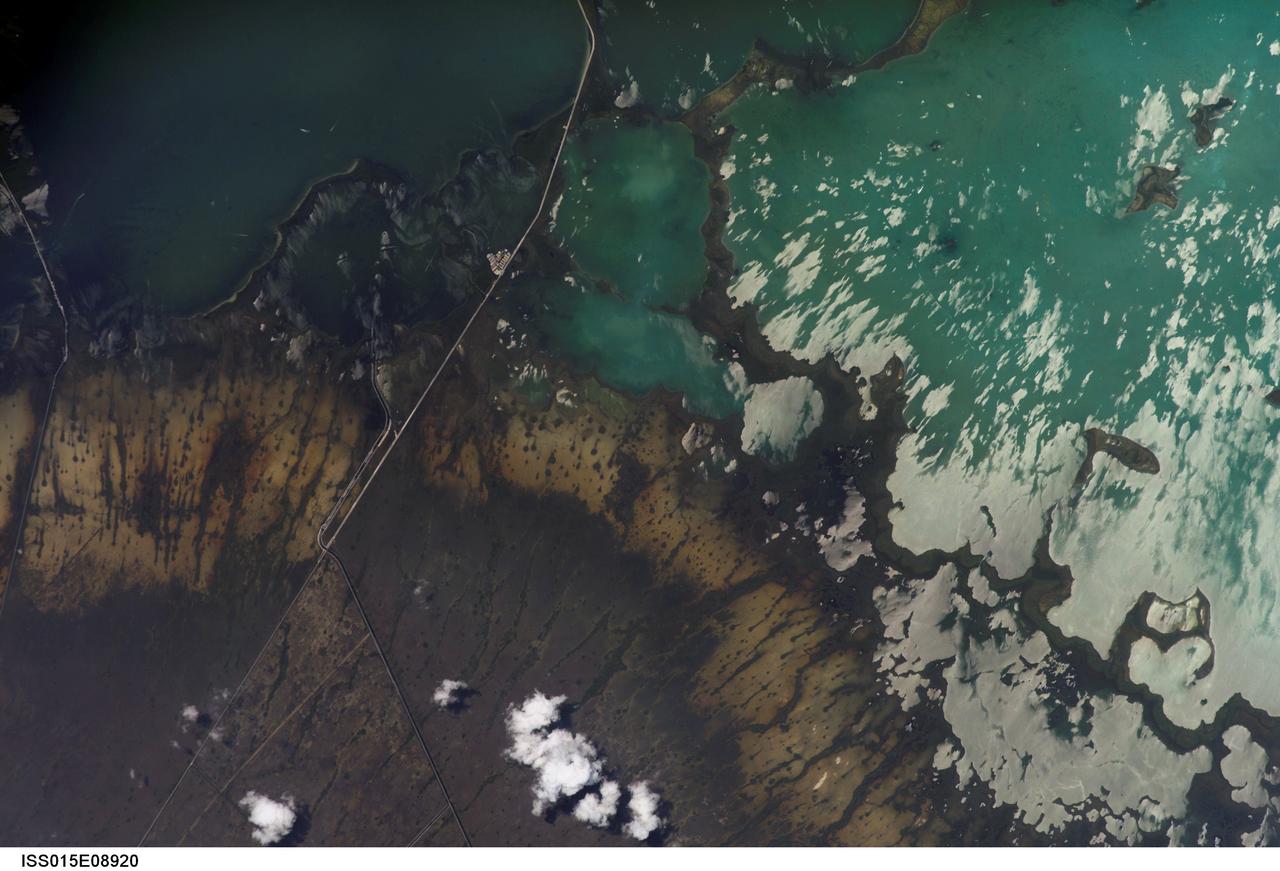 ISS015-E-08920 (19 May 2007) --- Southern Everglades National Park, Florida is featured in this image photographed by an Expedition 15 crewmember on the International Space Station. Everglades National Park in southern Florida is the largest subtropical wilderness in the United States. Known as the "river of grass", the Everglades wetlands and wooded uplands host a variety of endangered species including crocodiles, manatees, and panthers. During the late 19th and 20th centuries, the original 11,000 square miles of wetlands were viewed as useless swampland in need of reclamation. The success of reclamation efforts -- for agriculture and urban expansion in southern Florida -- has led to the loss of approximately 50 per cent of the original wetlands and 90 per cent of wading bird species. Today, an extensive restoration effort is underway to return portions of the Everglades to a more natural state and prevent further ecosystem degradation. This view highlights the southern Everglades estuarine ecosystem where the wetlands meet Florida Bay. Thin fingers of land and small islands (keys) host mangrove, hardwood hammocks, marsh and prairie (mainly dark to light green in the image). The tan and grayish-brown areas are dominantly scrub, marshland and prairie; small green "dots" and narrow lines in this region are isolated mangrove and hardwood stands indicating the general direction of slow water flow toward the bay. The silver-gray regions are water surfaces highlighted by sunglint. The roadway forming the western boundary of the National Park is US Route 1 connecting the Miami metropolitan area to the north (not shown) with the Florida Keys to the south (not shown). A small built feature visible along the roadway is a fishing camp.