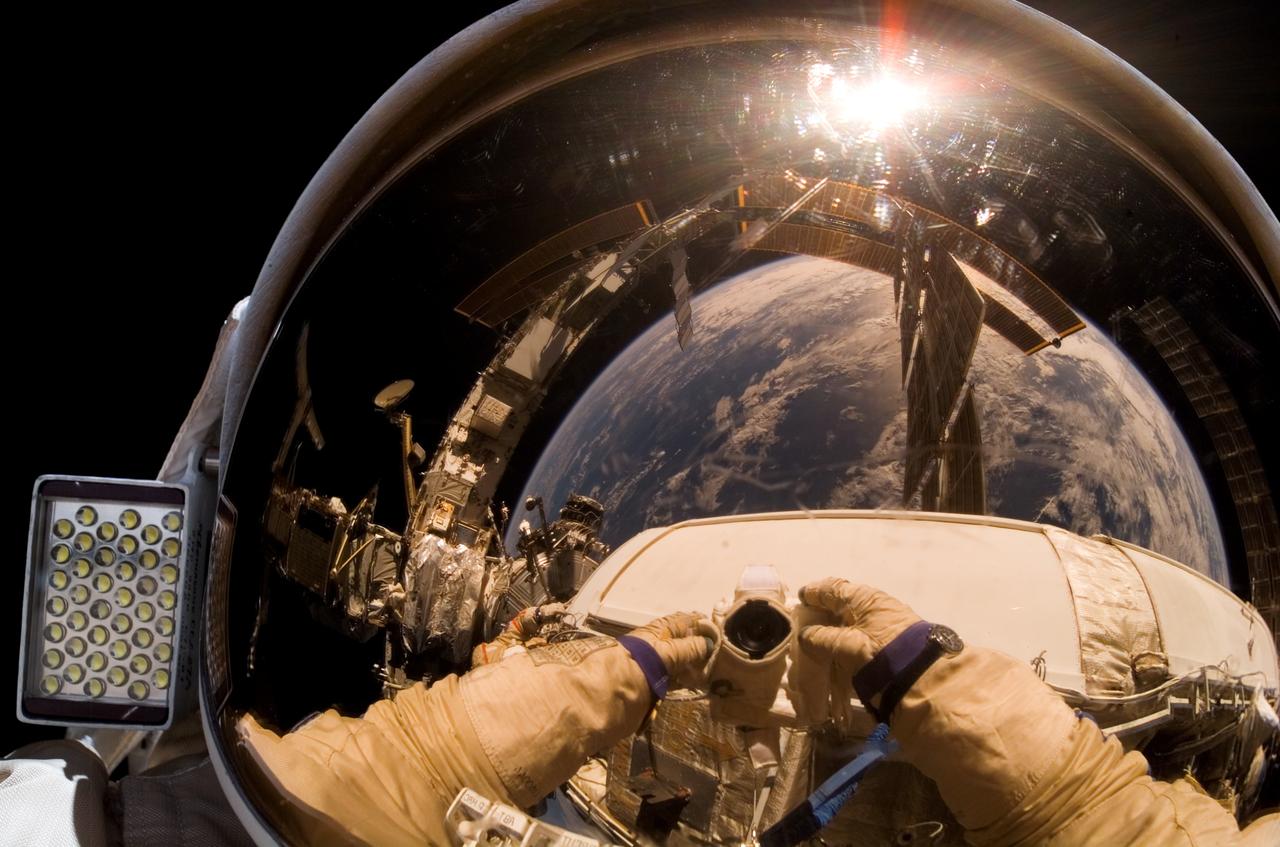 ISS015-E-10939 (6 June 2007) --- Cosmonaut Oleg V. Kotov, Expedition 15 flight engineer representing Russia's Federal Space Agency, wearing a Russian Orlan spacesuit, uses a digital still camera to expose a photo of his helmet visor during a session of extravehicular activity (EVA). With the Earth in the background, International Space Station solar array panels are also visible in the reflections. Among other tasks, Kotov and cosmonaut Fyodor N. Yurchikhin (out of frame), commander representing Russia's Federal Space Agency, completed the installation of 12 more Zvezda Service Module debris panels and installed sample containers on the Pirs Docking Compartment for a Russian experiment, called Biorisk, which looks at the effect of space on microorganisms.