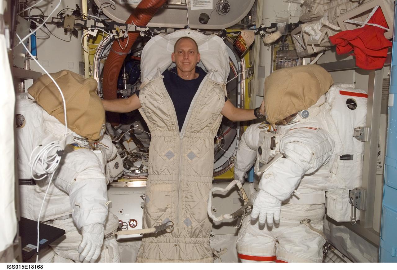 ISS015-E-18168 (11 July 2007) --- With most of his body tucked away in a sleeping bag, astronaut Clay Anderson, Expedition 15 flight engineer, poses for a photo near two extravehicular mobility unit (EMU) spacesuits in the Quest Airlock of the International Space Station.