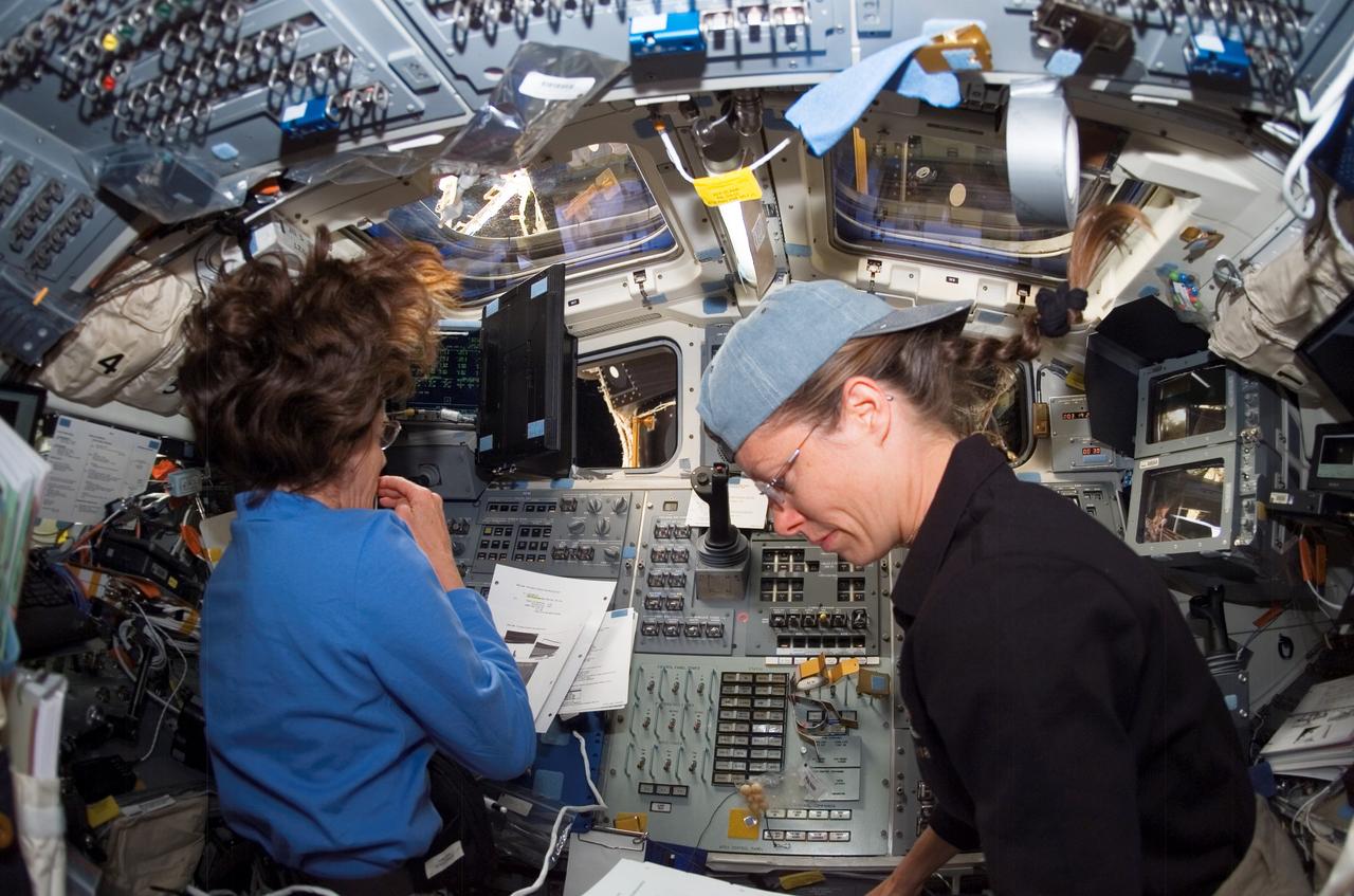 ISS015-E-22201 (12 Aug. 2007) --- During a focused inspection of apparent damage on the underside of the shuttle, astronauts Barbara R. Morgan (left) and Tracy Caldwell, both STS-118 mission specialists, work at the aft flight deck controls of Space Shuttle Endeavour while docked with the International Space Station.