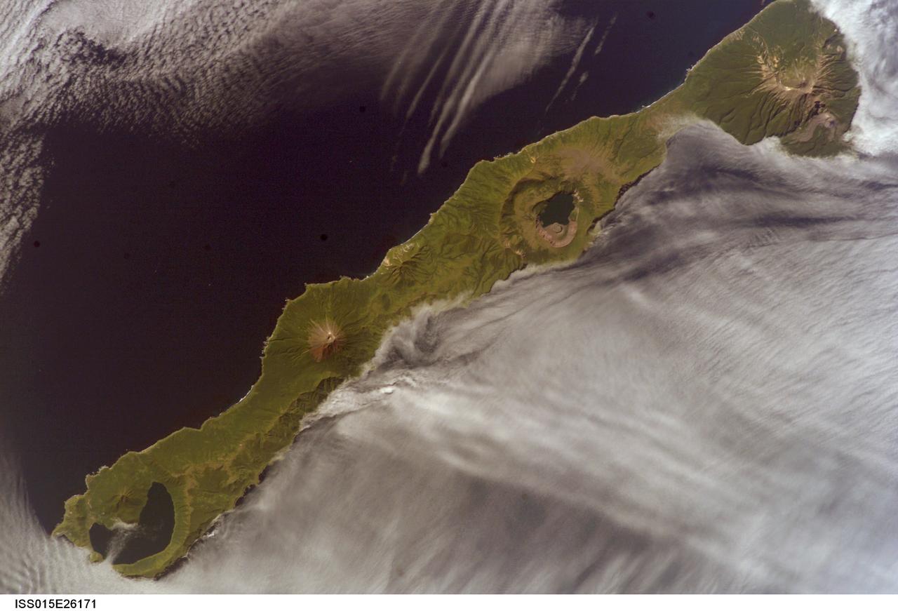 ISS015-E-26171 (1 Sept. 2007) --- Simushir Island, Kuril Archipelago, Russian Far East, is featured in this image photographed by an Expedition 15 crewmember on the International Space Station. Simushir is a deserted, 5-mile-wide volcanic island in the Kuril island chain, half way between northern Japan and the Kamchatka Peninsula of Russia.  Four volcanoes - Milne, Prevo, Urataman and Zavaritski - have built cones that are high enough to rise above the altitude of green forest. The remaining remnant of Zavaritski volcano is a caldera -- a structure formed when a volcano collapses into its emptied magma chamber. A small lake fills the innermost of three nested calderas which make up Zavaritski Caldera. The larger caldera of Urataman Volcano is connected to the sea. A defunct Soviet naval base occupies the northern tip of the island next to this caldera. The islands and volcanoes of the Kuril chain are part of the Pacific Rim of Fire, marking the edge of the Pacific tectonic plate. Low stratus clouds approaching from the northwest (from the Sea of Okhotsk--top left) bank up against the northwest side of the island, making complex cloud patterns. A small finger of cloud can be seen entering the northernmost caldera (Urataman) at sea level. When this image was taken, the cloud layer had stopped at the northwest coast of the island, not flowing over even the low points of the island between the volcanoes. The cloud pattern suggests that the air mass flowed up and over the island, descending on the southeast side. This descending motion was enough--under stable atmospheric conditions--to warm up the atmosphere locally so that a cloud-free zone formed on the southeastern, lee side of the island.