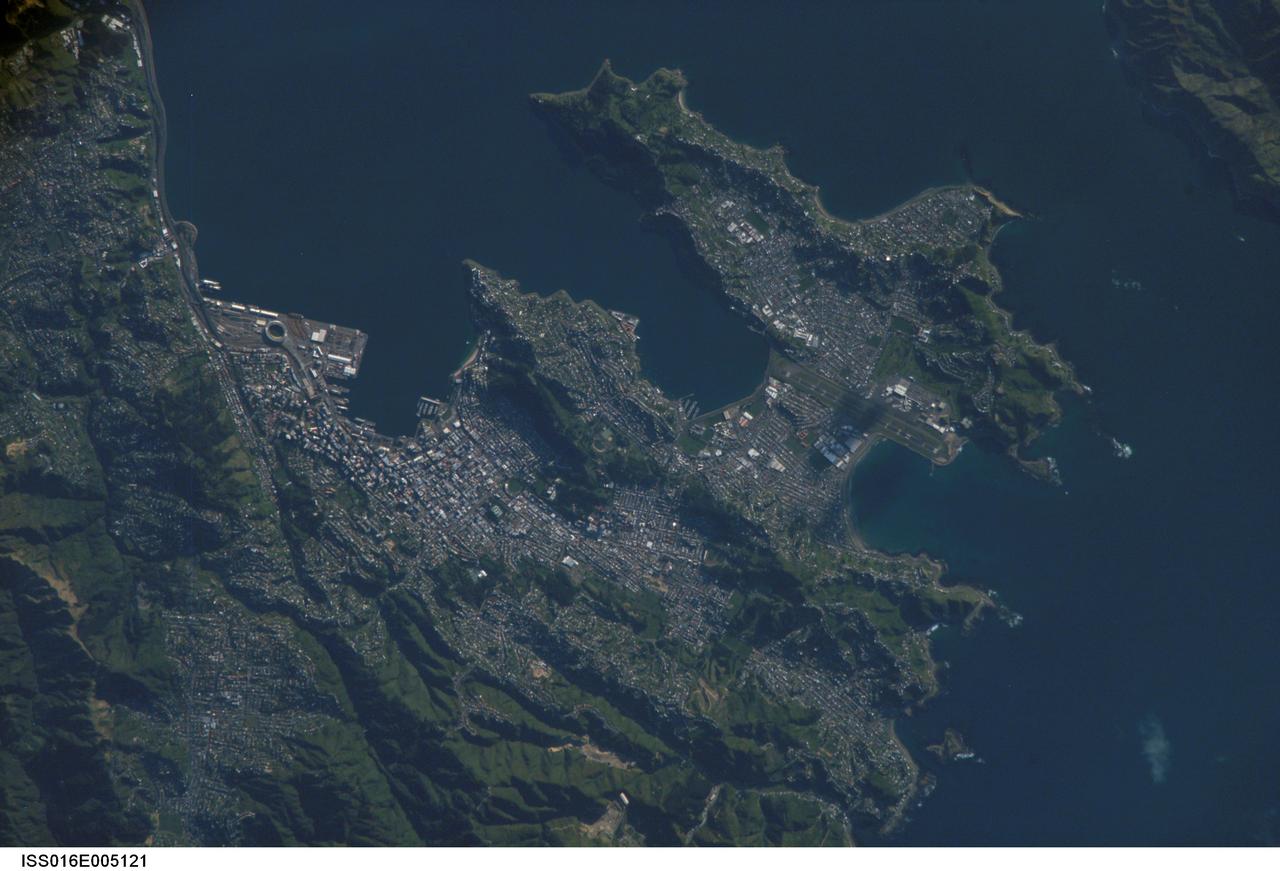 ISS016-E-005121 (21 Oct. 2007) --- Wellington, New Zealand is featured in this image photographed by an Expedition 16 crewmember on the International Space Station. New Zealand's capital of Wellington is located at the southwestern tip of North Island near the Cook Strait. The city is the second largest in New Zealand (after Auckland), and at 41 degrees south latitude, it is the southernmost capital city of the world. The North and South Islands of New Zealand are located along the active Australian-Pacific tectonic plate boundary -- the Islands are only a small part of a larger submerged fragment of continental crust. The glancing collision of these two tectonic plates results in uplift of the land surface, expressed as low hills on North Island and the Southern Alps on South Island. Local topography visible in this view is a result of these tectonic forces and weathering processes, which have exerted a strong influence on the morphology of the city. Tightly clustered white rooftops and high building density of the central business district are visible to the south of the Westpac Stadium between vegetated (green) northeast-southwest trending ridges. Lower density development (gray gridded regions with scattered white rooftops) has spread eastwards along the Miramar Peninsula. Five major faults that run through the Wellington metropolitan area; the largest magnitude earthquake recorded in New Zealand (approximately 8.2 on the Richter Scale) occurred in 1855 on one of these (the Wairarapa Fault). Recognition of the potential seismic hazard in the metropolitan area has led to adoption of building codes to maximize structural resistance to earthquake damage.