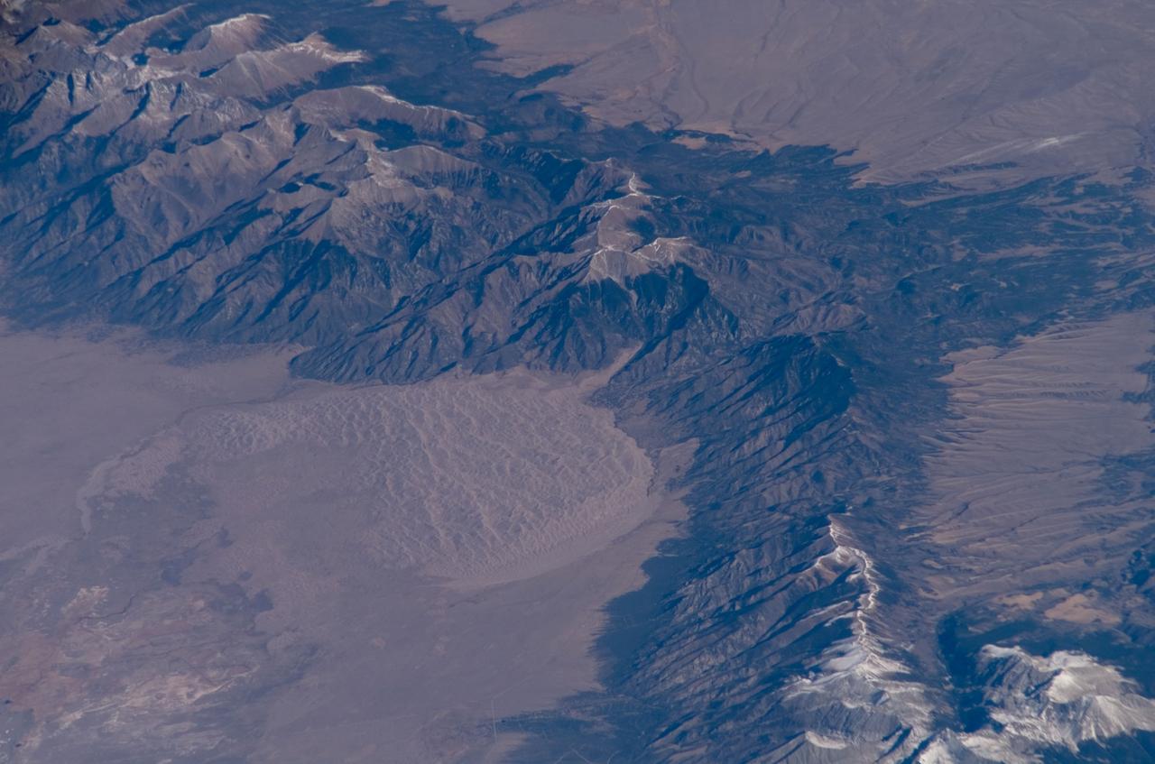 ISS016-E-006986 (26 Oct. 2007) --- Great Sand Dunes National Park and Preserve, Colorado is featured in this image photographed by an Expedition 16 crewmember on the International Space Station. The Sangre de Cristo Mountains of south-central Colorado stretch dramatically from top left to lower right of this image, generally outlined by the dark green of forests with white snow-capped peaks on the highest elevations. Dun-colored dunes, covering an area of 80 square kilometers, are banked up on the west side of the mountains and comprise the Great Sand Dunes National Park and Preserve. Originally established in 1932 as a National Monument, it was reauthorized as a National Park in 2004. The park contains dunes over 750 feet (227 meters) high -- among the highest in North America. Sand grains that make up the dunes are small enough to be moved along by the wind (a process known as saltation), although much of the dunefield is now anchored by vegetation. Predominant winds blow broadly to the east, so that sand in the San Luis valley (part of which appears at lower left) is driven towards and piled against the Sangre de Cristo Mts. The sand of the dunes is mostly derived from ancient exposed lakebed sediments - now the floor of the San Luis valley - formed by erosion of rocks in the Sangre de Cristo and San Juan Mountains (located to the west). The action of streams and occasional storms today returns some of the impounded sand back to the valley, where the prevailing winds begin the sand's migration to the dunefield anew. Interestingly, the specific location of the sand field appears to be related to a locally lower altitude sector of the Sangre de Cristo Mts. Altitudes can be inferred from the distribution of snow cover on the day this image was taken. Areas to the north (Cleveland Peak and northward) of the dunefield, and to the south around Blanca Peak, are higher than the ridgeline next to the dune field where almost no snow is visible. Since winds are preferentially channeled over the lower parts of any range (hundreds of meters lower here than ridgelines to north and south), sand grains are carried up to (but not over) the low point of the range.