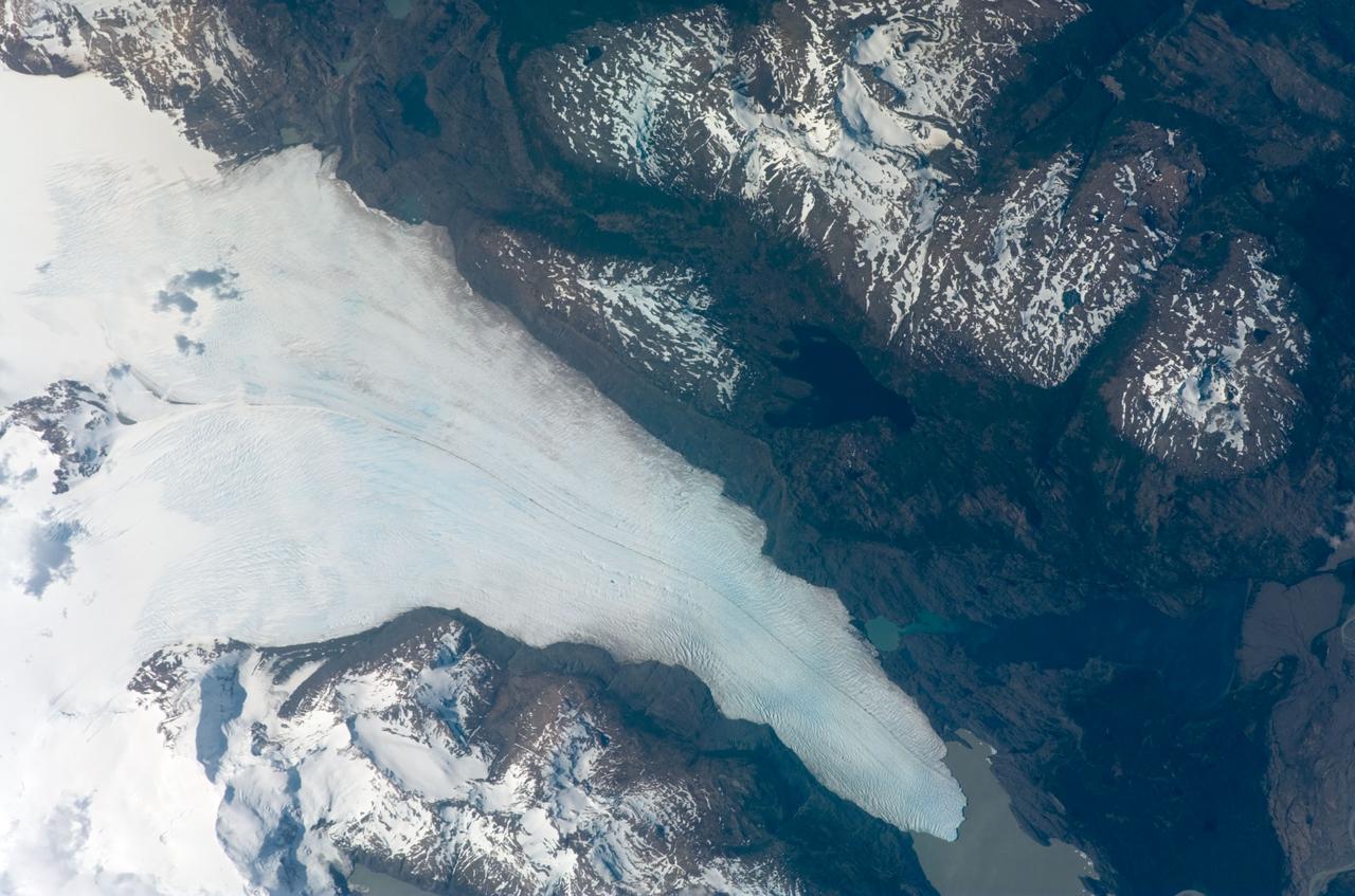ISS016-E-012047 (22 Nov. 2007) --- Tyndall Glacier, located in the Torres del Paine National Park in Chile, is featured in this image photographed by an Expedition 16 crewmember on the International Space Station. This glacier, which has a measured total area of 331 square kilometers and length of 32 kilometers (1996 measurements), begins in the Patagonian Andes Mountains to the west and terminates in Lago Geikie. A medial moraine is visible in the center of the glacier, extending along its length (center left). These accumulations of soil and rock debris form along the edges of a glacier as it flows downhill across the landscape (much like a snowplow builds ridges of snow along the roadside). Glaciers flowing downslope through adjacent feeder valleys merge when they encounter each other, and debris entrained along their sides becomes concentrated in the central portion of the new combined ice mass -- much as small streams join to form a river. Crevasse fields are also visible in the image. The crevasses -- small, but potentially quite deep fissures -- form as a result of stress between slower- and faster-moving ice within the glacier. Crevasse fields on Tyndall Glacier are most evident near rock promontories extending into the glacier -- causing the ice to slow as it flows around the obstruction.