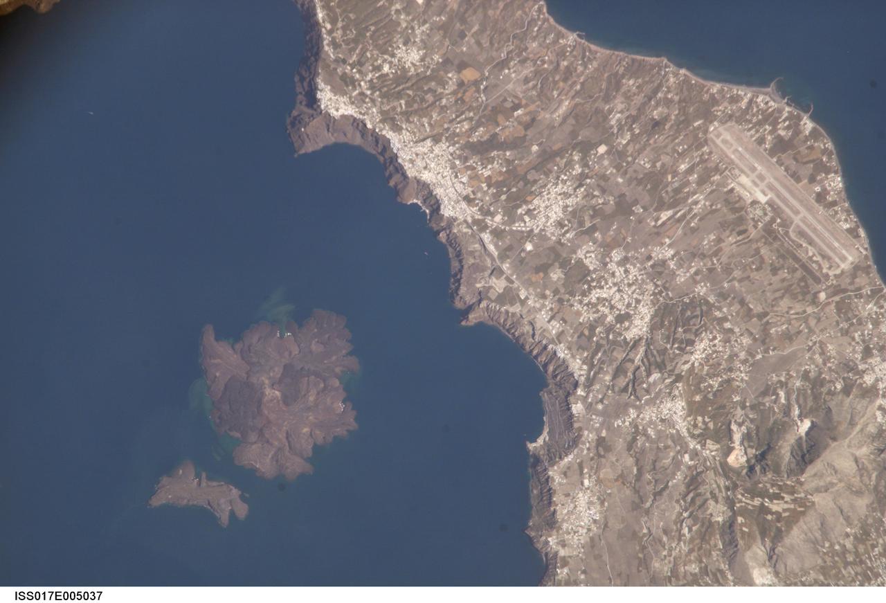 ISS017-E-005037 (19 April 2008) --- Santorini Volcano, Greece is featured in this image photographed by an Expedition 17 crewmember on the International Space Station. According to scientists, one of the largest volcanic eruptions in the past 10,000 years occurred approximately 1620 BC on the volcanic island of Santorini in the Aegean Sea. This view illustrates the center of Santorini Volcano, located approximately 118 kilometers to the north of Crete (not shown). Prior to 1620 BC, the island of Santorini -- now known as Thera -- had been built up by layers of lava created by overlapping shield volcanoes, and had experienced three significant eruptions that formed overlapping calderas, or collapsed magma chambers. Around 1620 BC, the fourth (and latest) major eruption created the present-day islands and caldera bay of Santorini Volcano. The caldera rim is clearly visible in this image as a steep cliff forming the western shoreline of the island of Thera. Following the 1620 BC eruption, much of the previous island of Santorini was destroyed or submerged. The white rooftops of cities and towns trace the caldera rim on the island of Thera, and overlook the young central islands of Nea Kameni and Palaea Kameni -- both, according to scientists, formed from lava domes and flows that started erupting approximately 1400 years after the last major caldera-forming event. Several of these flows are visible in the image as brown to dark-brown irregular masses forming Nea Kameni (left). The most recent volcanic activity in the Kameni islands occurred in 1950, and included some small explosions and production of lava. The extent of development and location of an airport (upper right) on Thera illustrate the popularity of Santorini Volcano as a tourist destination. Today, volcanic activity is closely monitored by the Institute for the Study and Monitoring of the Santorini Volcano, or ISMOSAV.