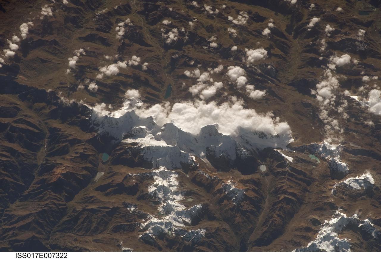 ISS017-E-007322 (17 May 2008) --- Cordillera Huayhuash in the Peruvian Andes is featured in this image photographed by an Expedition 17 crewmember on the International Space Station. This view was taken looking east as the station was flying approximately 100 kilometers off the Peruvian coast and shows Cordillera Huayhuash (pronounced Why-wash). Here clouds are banked up on the east side, snow covers all higher slopes and mountain peaks, and glaciers occupy lower slopes. This prominent but short mountain range (25 kilometers in length) boasts twenty peaks of remarkable steepness and ridge sharpness. Although only 100 kilometers from the coastline, six of the peaks reach above 6,000 meters (more than 19,500 feet), the highest of which is Nevado Yerupaja, Peru's second highest peak, variously estimated as 6,617 and 6,635 meters high. Generally considered the most spectacular peak in South America, Yerupaja is so steep that it has seldom been climbed. The best climbing approach is from the southwest, the face seen in this view. Yerupaja is locally known as El Carnicero (The Butcher) because of its blade-like ridges, features typical of mountains that have been heavily eroded by glacial ice. Other features created by the erosive effect of flowing ice are small glacial lakes, which often vary in color due to different amounts of fine mud being fed into them by meltwater from under the glaciers. According to scientists, during the ice ages the glaciers advanced many kilometers outward from the cordillera, occupying all the surrounding valley floors (all of which lie above 3,000 meters) producing the characteristic U-shaped valleys.