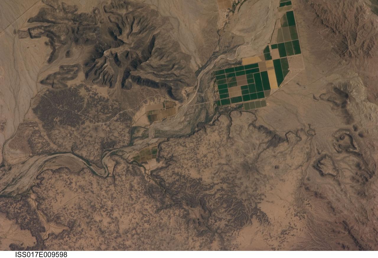 ISS017-E-009598 (18 June 2008) --- The Sentinel Volcanic Field in Arizona is featured in this image photographed by an Expedition 17 crewmember on the International Space Station. This detailed view depicts a portion of the Gila River channel (center) between the Sentinel Volcanic Field and Oatman Mountain in south-central Arizona. The northernmost boundary of the Sentinel field is visible in the image, recognizable by the irregular flow fronts, or leading edge, of thin basalt lava flows erupted from low volcanic cones approximately 3.3--1.3 million years ago, according to scientists. Coloration of the lava flow tops ranges from dark brown exposed rock to a tan, carbonate-rich soil cover. Active agricultural fields along the Gila River are a rich green set against the surrounding desert. In contrast to the gentle topography of the Sentinel Volcanic Field, Oatman Mountain (upper left) rises from the Gila River channel to an elevation of approximately 560 meters. While Oatman Mountain is located close to the Sentinel field, it represents an earlier phase of volcanic activity in the area. Volcanic rocks comprising Oatman Mountain were more viscous, leading to shorter, stronger flows that are weathered into stream channels and scarps on the mountain slopes. The mountain is a popular hang gliding destination due to abundant thermal currents rising from the surrounding desert floor and lava surfaces.