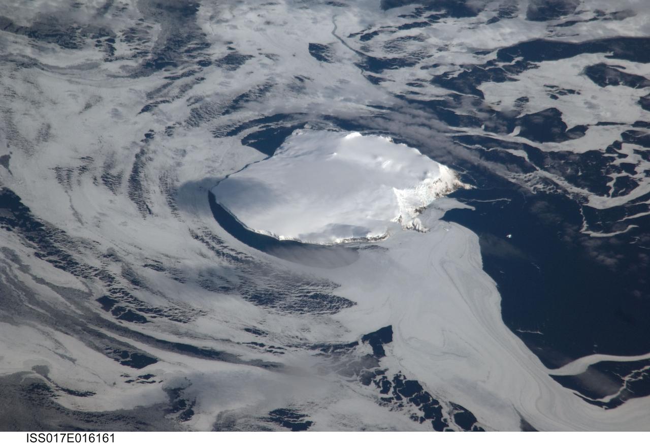 ISS017-E-016161 (13 Sept. 2008) --- Bouvet Island in the South Atlantic Ocean is featured in this image photographed by an Expedition 17 crewmember on the International Space Station. Bouvet Island is known as the most remote island in the world. Antarctica, over 1600 kilometers to the south, is the nearest land mass. Located near the junction between the South American, African, and Antarctic tectonic plates, the island is mostly formed from a shield volcano -- a broad, gently sloping cone formed by thin, fluid lavas -- that is almost entirely covered by glaciers. The prominent Kapp (Cape) Valdivia on the northern coastline is a peninsula formed by a lava dome -- a volcanic feature built by viscous lavas with a high silica content. It is only along the steep cliffs of the coastline that the underlying dark volcanic rock is visible against the white snow and ice blanketing the island. Bouvet Island was discovered by the French Captain Lozier-Bouvet in 1739, and was subsequently visited by representatives of different nations several times during the 19th century. The island was annexed by the Kingdom of Norway in 1927 following a Norwegian expedition's stay on the island. Bouvet is uninhabited, and its extremely harsh environment precludes anything but short-duration stays. Nevertheless, the island supports some flora (such as lichens) and fauna (seabirds and seals). Abundant sea ice surrounds the island in this view (center).