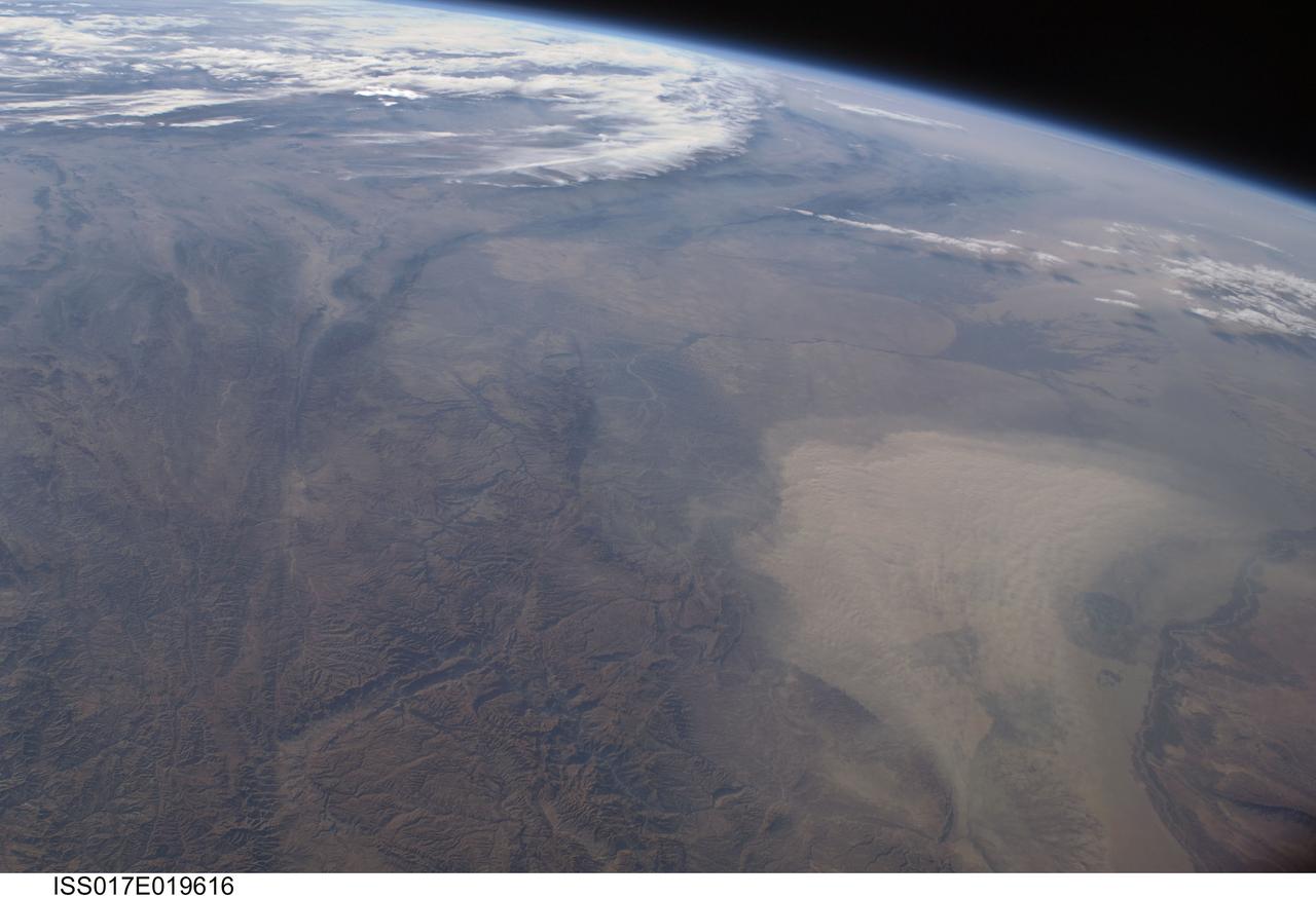 ISS017-E-019616 (16 Oct. 2008) --- A dust storm in Turkmenistan, Central Asia is featured in this image photographed by an Expedition 17 crewmember on the International Space Station. This west-looking view, taken with a short focal length lens from the station, shows a wide swath of central Asia--from Afghanistan, along the length of Turkmenistan to the Caspian Sea. Winds blowing down the largest river valley in the region, the Amudarya, were strong enough to raise a large dust storm. Dust appears as a light brown mass extending into the center of the image from the lower right. Diffuse dust from prior windy weather appears over much of the area making a regional haze that clouds much of the landscape detail. The haze partly obscures the irrigated agriculture in Turkmenistan and entirely obscures the Caspian Sea. Numerous rivers rise in the Hindu Kush mountain complex (lower left). The Band-i Amir River is a major tributary of the main regional river, the Amudarya, which it reaches via a deep canyon. The Amudarya River was the major historical contributor of water to the Aral Sea, but today extensive diversion of river water for agricultural purposes has lead to extensive exposure and desiccation of the sea bed. The exposed sea bed is a major source of saline dusts contaminated with agricultural chemicals that pose a significant environmental hazard to central Asia. To a lesser extent, dusts are also mobilized from sediments along the Amudarya river channel. The Paropamisus Range and the Amudarya (also known as the Oxus River) are mentioned in histories of Alexander the Great's famous military expedition from Greece to India. His horsemen made a fast side excursion from near the Caspian Sea (top right) as far as the Amudarya (lower right).