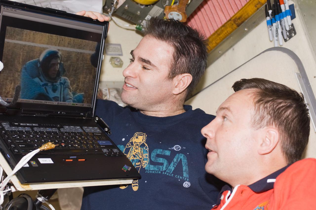 ISS018-E-005026 (23 Oct. 2008) --- Astronaut Greg Chamitoff (left) and cosmonaut Yury Lonchakov, both Expedition 18 flight engineers, watch live video of post landing activities on the steppes of Kazakhstan of Expedition 17 crewmembers and spaceflight participant on a computer screen in the Zvezda Service Module of the International Space Station. Cosmonaut Sergei Volkov, Expedition 17 commander, is visible on the screen.