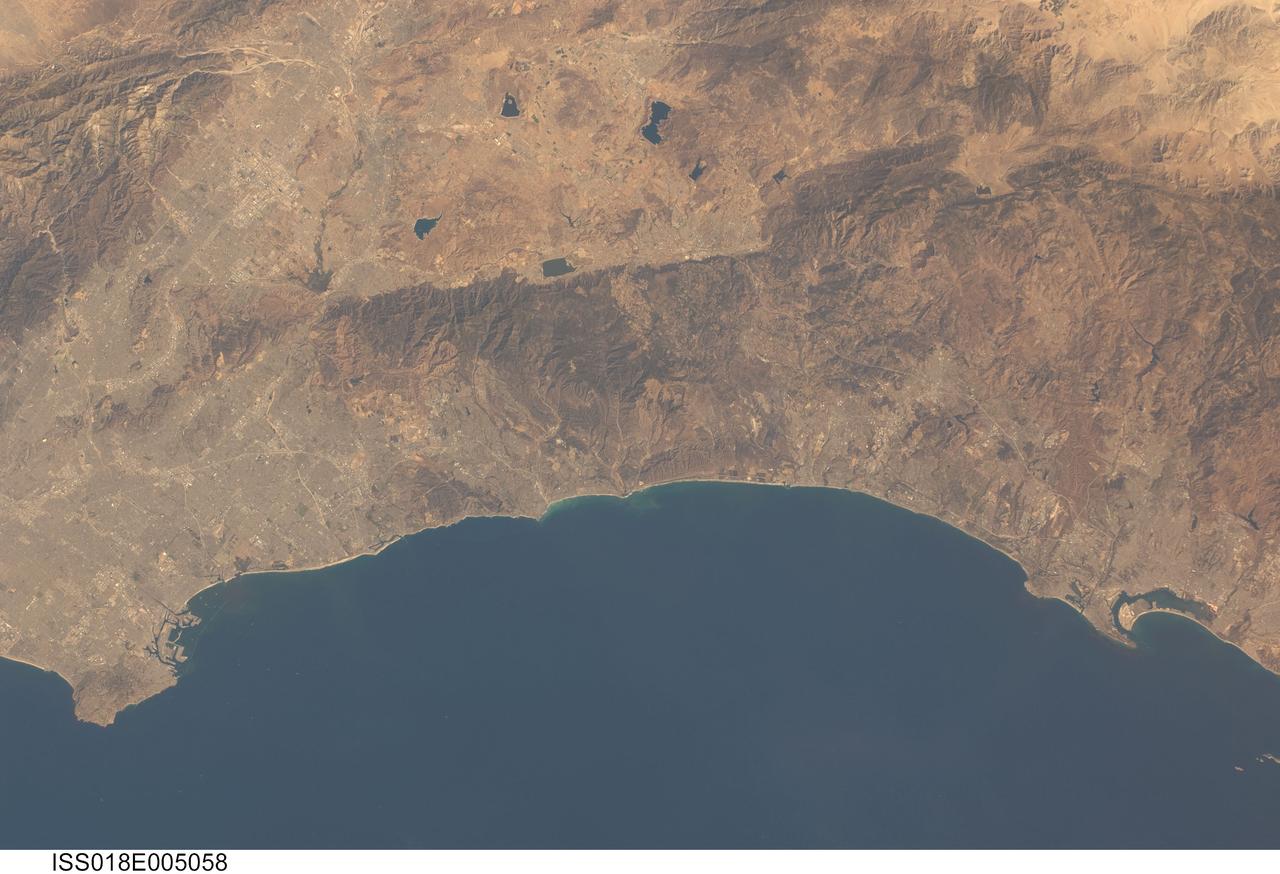 ISS018-E-005058 (24 Oct. 2008) --- Southern California's coastline, from southern Los Angeles to Tijuana in Mexico, a distance of about 225 kilometers, is featured in this image photographed by an Expedition 18 crewmember on the International Space Station. Port facilities of Los Angeles Harbor give much detail to the coastline at the north end and arcuate San Diego Bay is highly recognizable at the south end (right bottom). The image includes much of one of the most densely populated parts of the USA, with approximately 20 million people within the parts of five counties shown here. The dense urban areas appear gray, with the largest conurbation in the north of the view, in the region Long Beach--Los Angeles--San Bernardino. A smaller zone appears around San Diego--Tijuana in the south. Major highways with their associated strip development snake through these dense urban areas. The geography and geomorphology of Southern California is defined by long linear features that are surface traces of large transform faults. These faults, including the Elsinore fault and San Jacinto fault seen here, are generally considered part of the San Andreas system, and make up the broad zone comprising the tectonic plate boundary between North America to the east and the Pacific plate to the west. The Elsinore fault marks the steep eastern scarp of the Santa Ana Mountains, as well as the precipitation boundary between the wetter mountains and the drier deserts to the east. The rainfall difference is reflected in the darker appearance (more vegetation) of the mountains and coastal regions. Inland of the mountains, climates are far drier, and the natural vegetation is scrubby and much less dense which allows brown and yellow soils to show through. However, the entire region is arid; water management is a critical issue for the large urban areas of the state. Several reservoirs that are visible east of the Santa Ana Mountains provide water for both cities and agriculture in southern California.