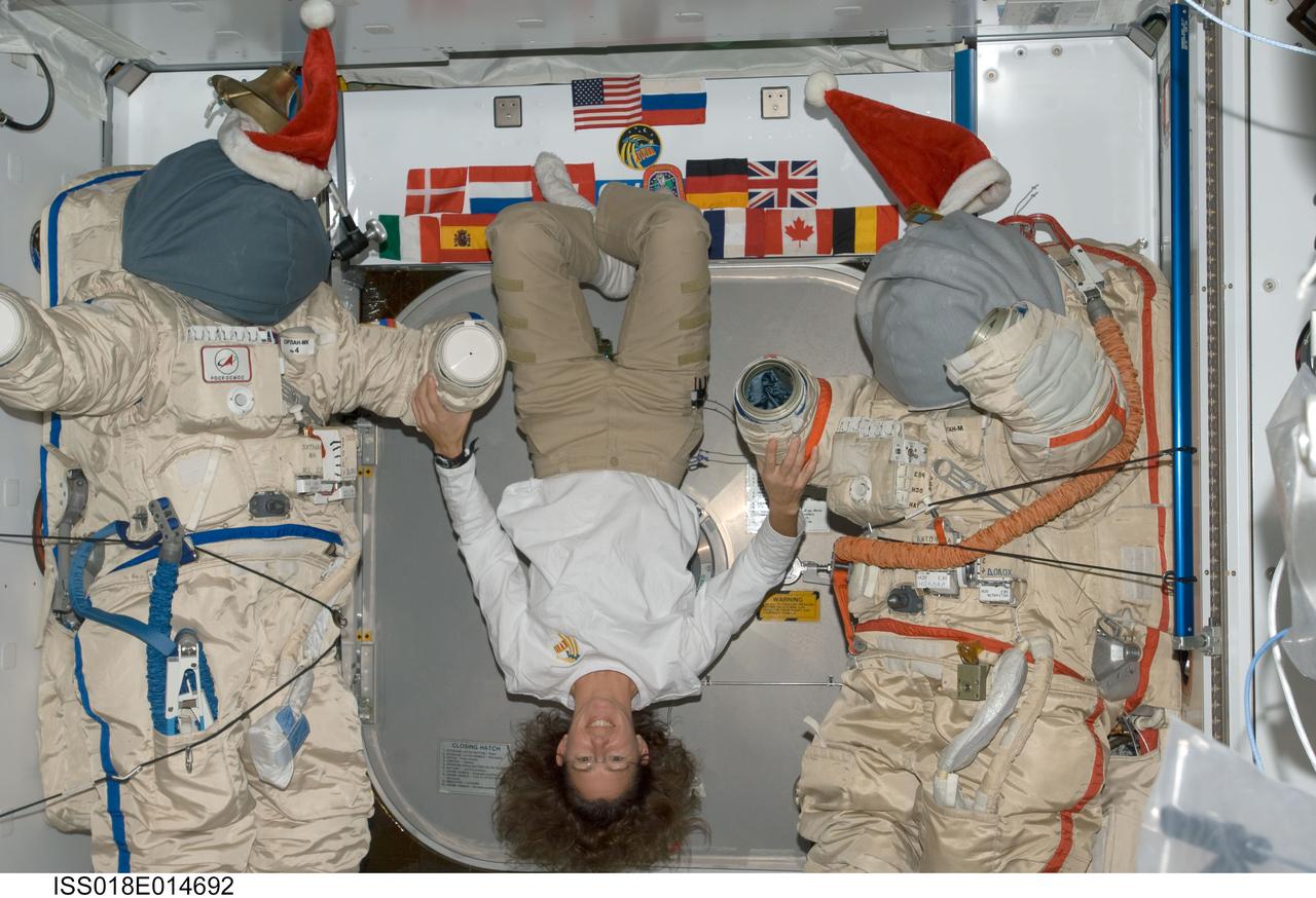 ISS018-E-014692 (23 Dec. 2008) --- Astronaut Sandra Magnus, Expedition 18 flight engineer, floats between two Russian Orlan spacesuits with Santa hats in the Harmony node of the International Space Station.
