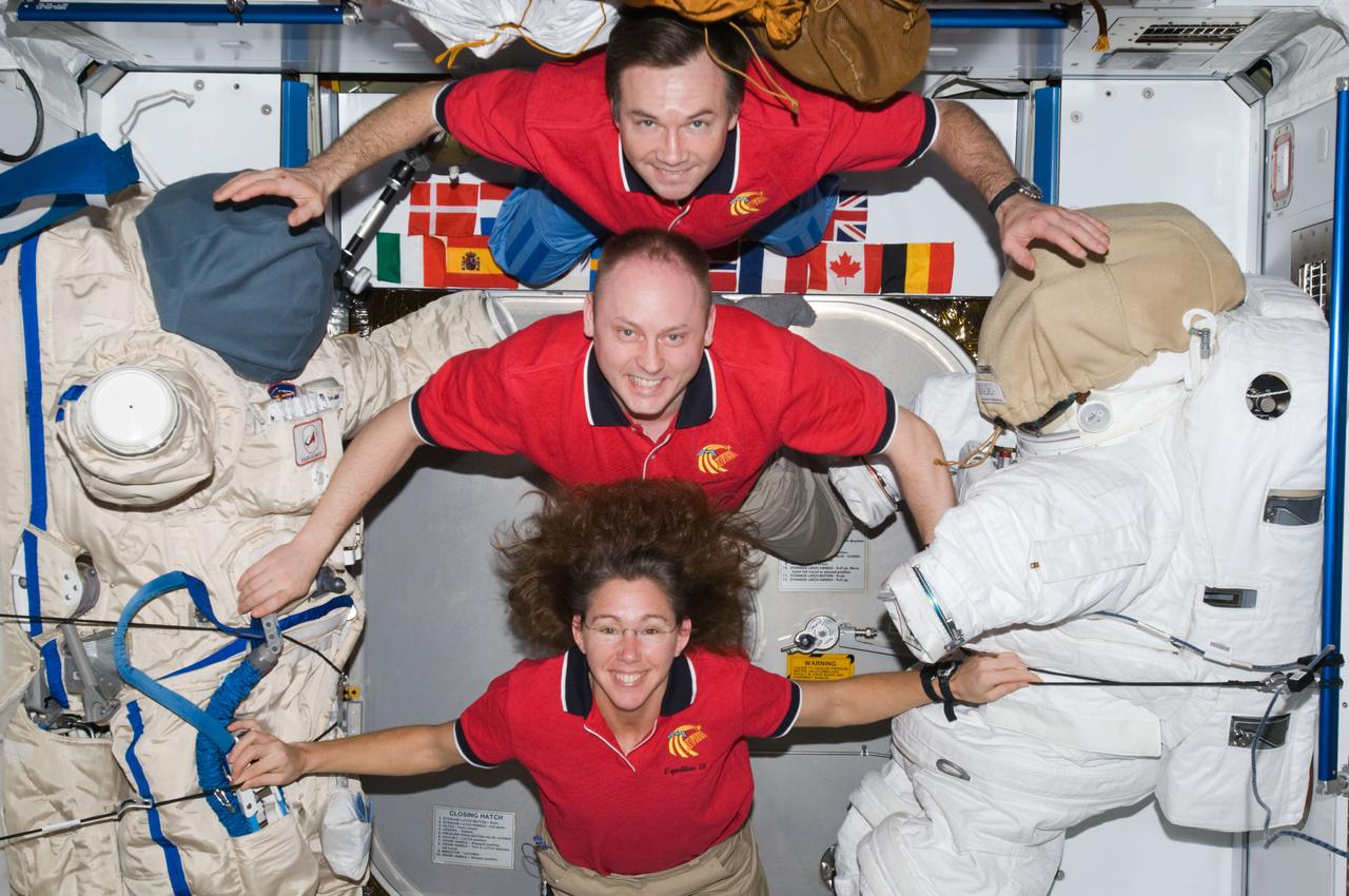 ISS018-E-033774 (19 Feb. 2009) --- Astronaut Michael Fincke (center), Expedition 18 commander; astronaut Sandra Magnus and cosmonaut Yury Lonchakov, both flight engineers, pose for a crew photo between a Russian Orlan spacesuit and an Extravehicular Mobility Unit (EMU) spacesuit in the Harmony node of the International Space Station.