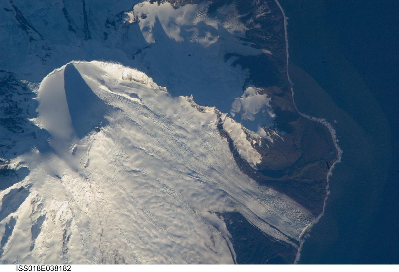 ISS018-E-038182 (28 Feb. 2009) --- Mawson Peak, Heard Island is featured in this image photographed by an Expedition 18 crewmember on the International Space Station. Heard Island is located in the southern Indian Ocean, approximately 1,550 kilometers to the north of Antarctica. The island is a visible part of the Kerguelen Plateau, a submerged feature on the seafloor formed by large amounts of volcanic rock erupted over a geologically short time period within an oceanic tectonic plate ? features like these are termed large igneous provinces by geologists. Most of Heard Island is formed from volcanic rocks associated with the Big Ben stratovolcano. The northeastern slopes of the volcano are visible in shadow at the top left of this detailed astronaut photograph. Recent observed volcanic activity at Heard Island has occurred at 2,745 meters high Mawson Peak, which sits within a breached caldera (collapsed and empty magma chamber beneath a volcano) on the southwestern side of the Big Ben volcano ? the shadow cast by Mawson Peak in the image points directly to the crescent-shaped caldera rim. Detailed geologic study of the Big Ben volcano is made difficult by the presence of several glaciers, including Gotley and Lied Glaciers on the southwestern slopes. This image, taken during Southern Hemisphere summer, also reveals some of the non-glaciated, light to dark brown volcanic rock forming the island on either side of Gotley Glacier.