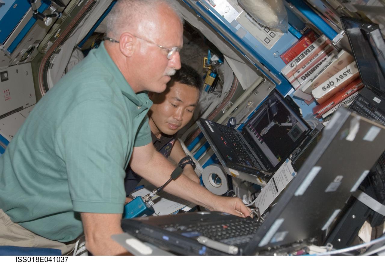 ISS018-E-041037 (18 March 2009) --- NASA astronaut John Phillips (foreground), STS-119 mission specialist; and Japan Aerospace Exploration Agency (JAXA) astronaut Koichi Wakata, Expedition 18 flight engineer, work the controls of the station's robotic Canadarm2 in the Destiny laboratory of the International Space Station while Space Shuttle Discovery remains docked with the station.