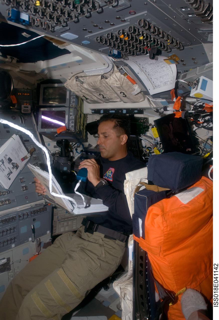 ISS018-E-041142 (19 March 2009) --- Astronaut Joseph Acaba (right), STS-119 mission specialist, looks over a checklist while using a communication system on the flight deck of Space Shuttle Discovery while docked with the International Space Station.