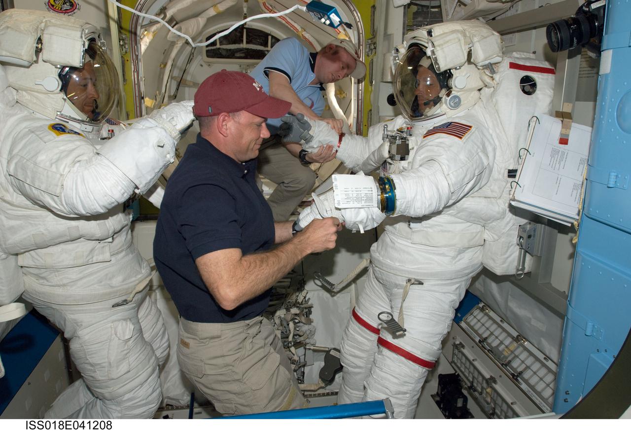 ISS018-E-041208 (19 March 2009) --- Astronauts Steve Swanson (right) and Richard Arnold, both STS-119 mission specialists, attired in their Extravehicular Mobility Unit (EMU) spacesuits, are pictured in the Quest Airlock of the International Space Station as the mission's first scheduled session of extravehicular activity (EVA) draws to a close. Astronauts Michael Fincke (center background), Expedition 18 commander; and Tony Antonelli, STS-119 pilot, assist with the doffing of the spacesuits.