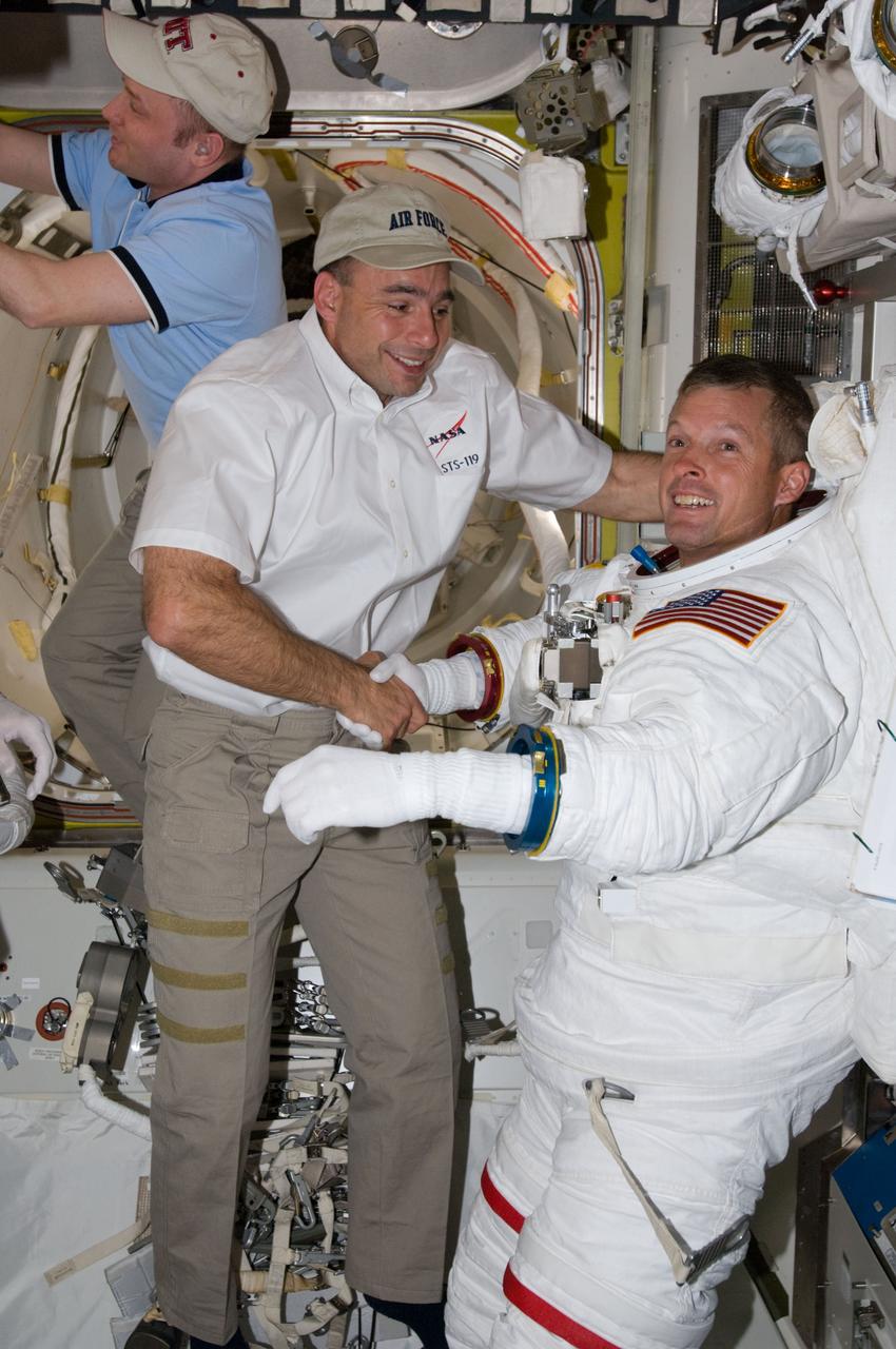 ISS018-E-041234 (19 March 2009) --- Astronaut Steve Swanson, STS-119 mission specialist, attired in his Extravehicular Mobility Unit (EMU) spacesuit, and astronaut Lee Archambault, STS-119 commander, shake hands in the Quest Airlock of the International Space Station as the mission's first scheduled session of extravehicular activity (EVA) draws to a close. Astronaut Michael Fincke, Expedition 18 commander, is visible at top left.